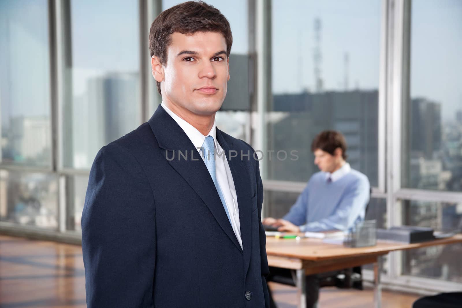 Portrait of confident male executive standing with colleague working in background