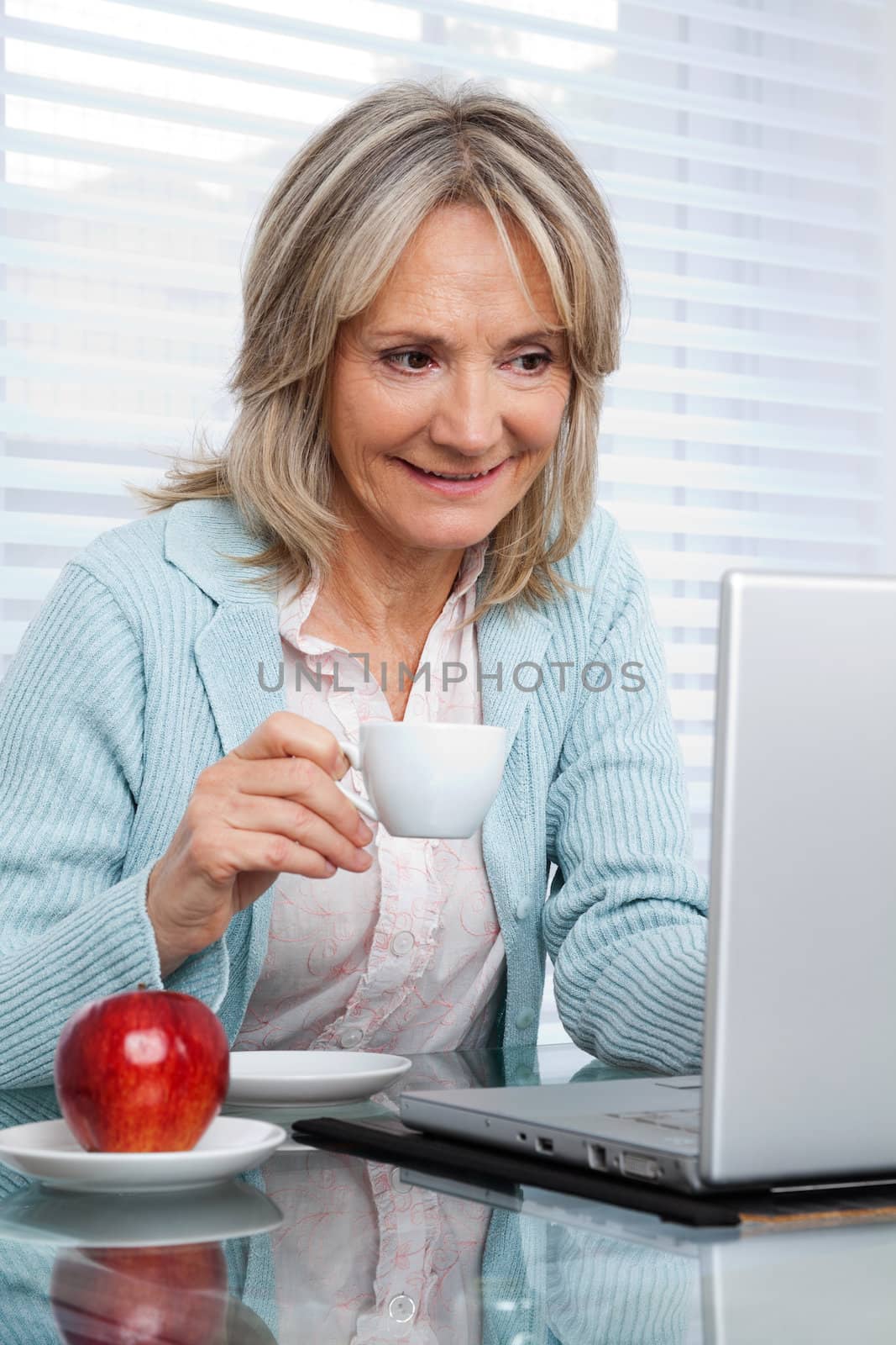 Smiling mature woman working on laptop while having cup of tea