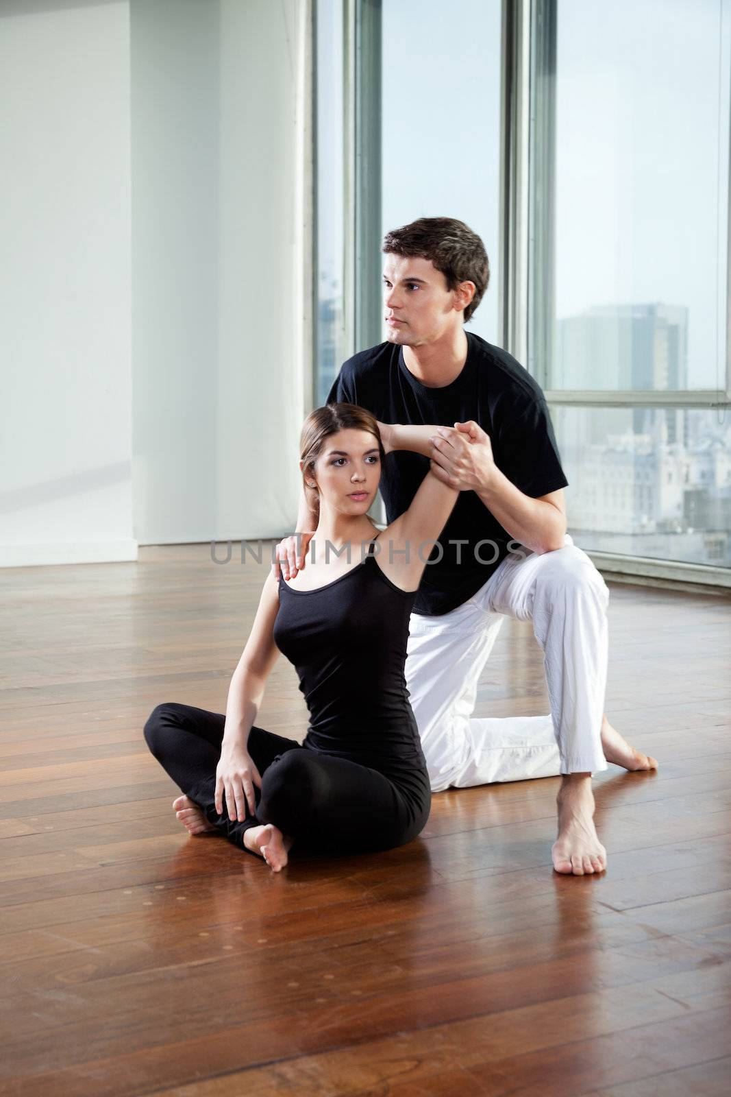 Yoga male instructor teaching yoga positions to young woman at gym