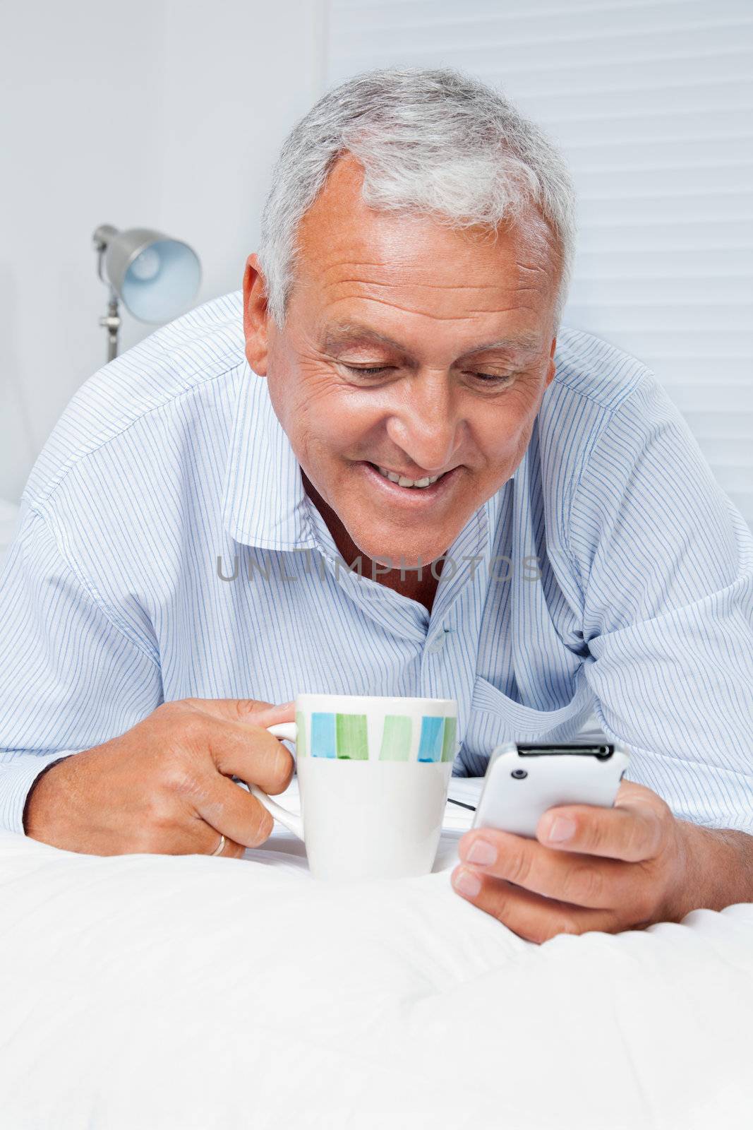 Smiling senior man using cell phone while having tea