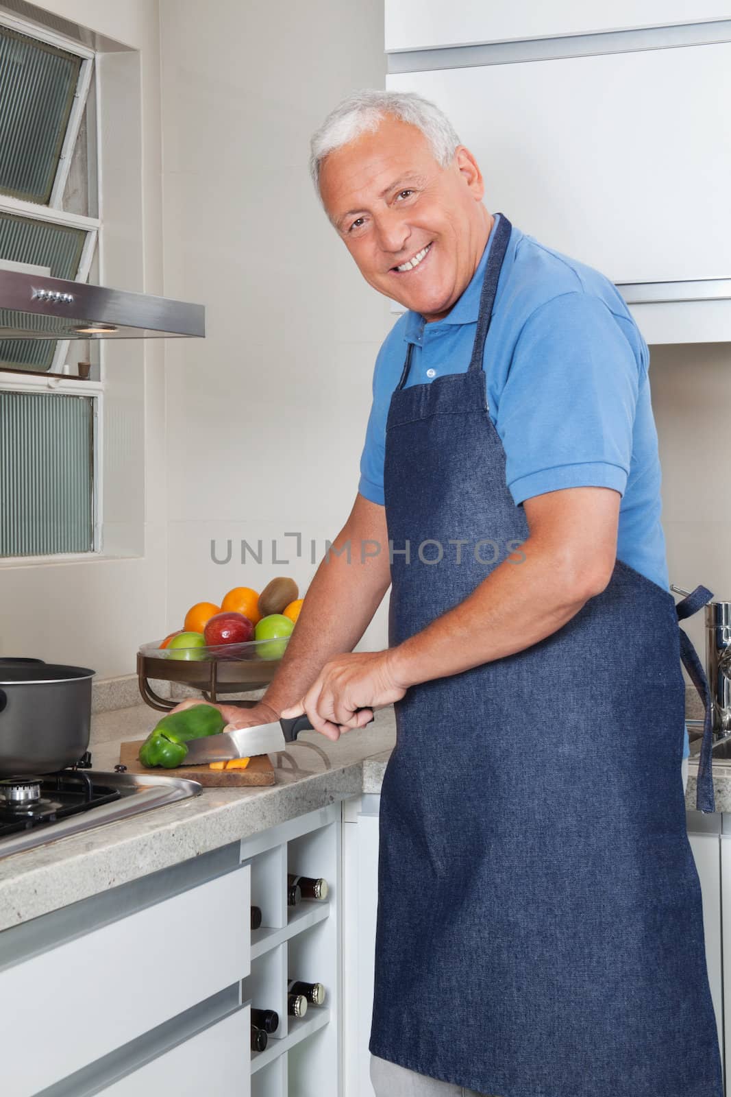 Portrait of smiling senior man cutting vegetables at kitchen counter