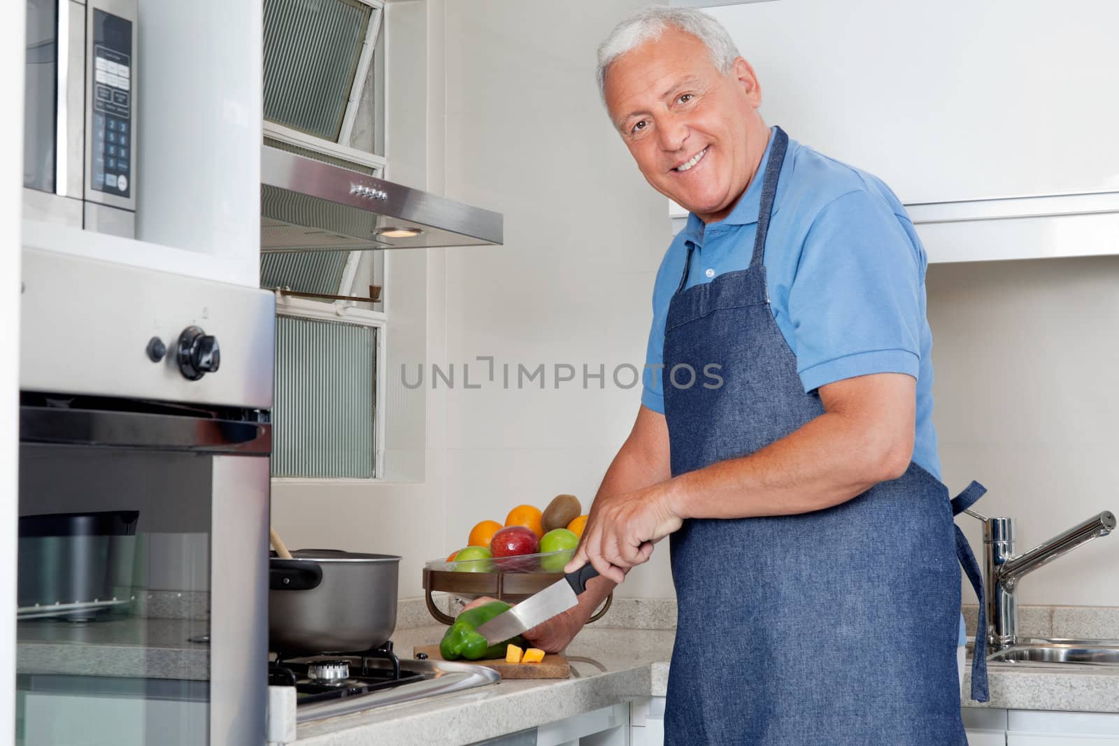 Portrait of happy senior man cutting vegetables at kitchen counter at home