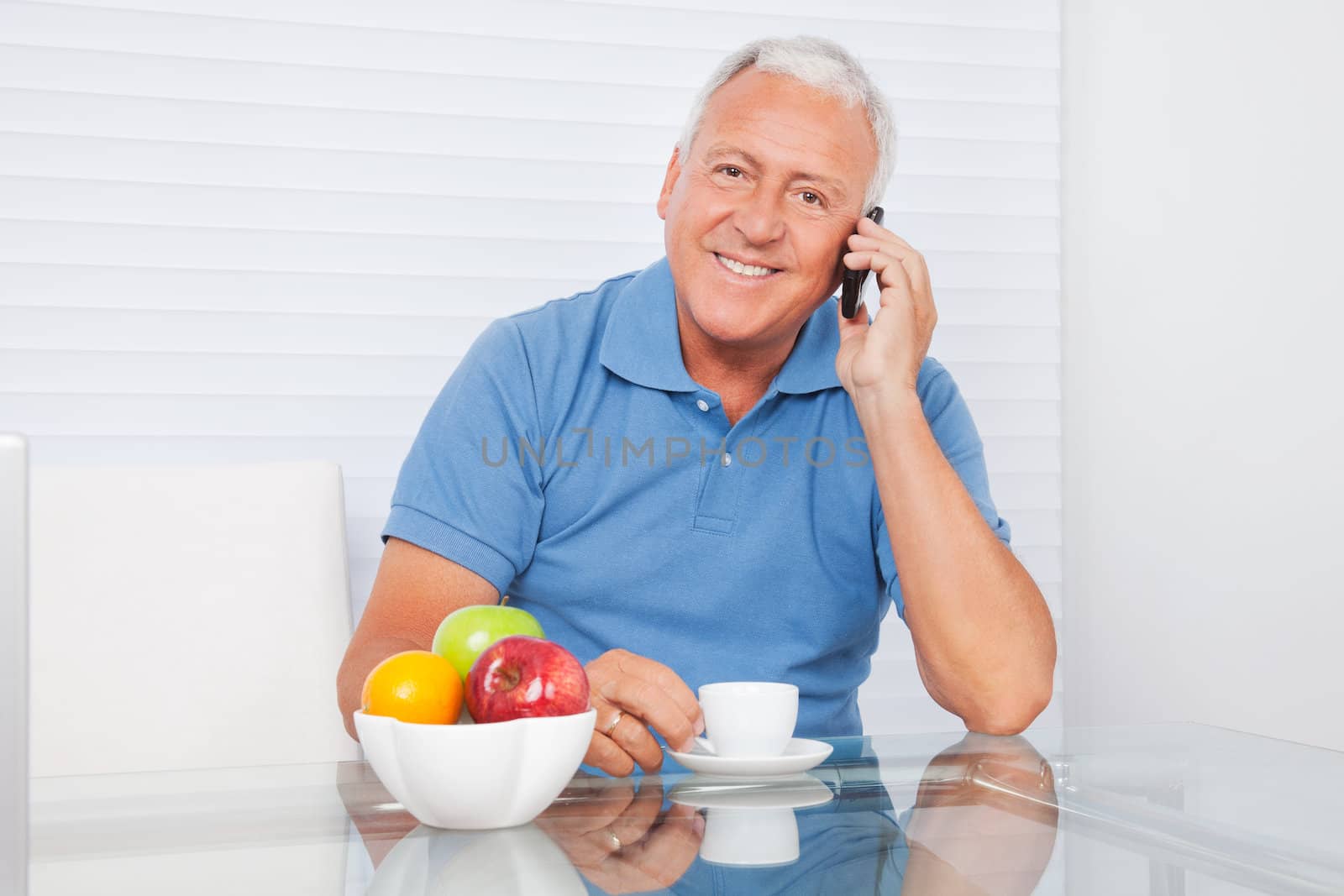 Portrait of smiling senior man talking on cell phone while having tea