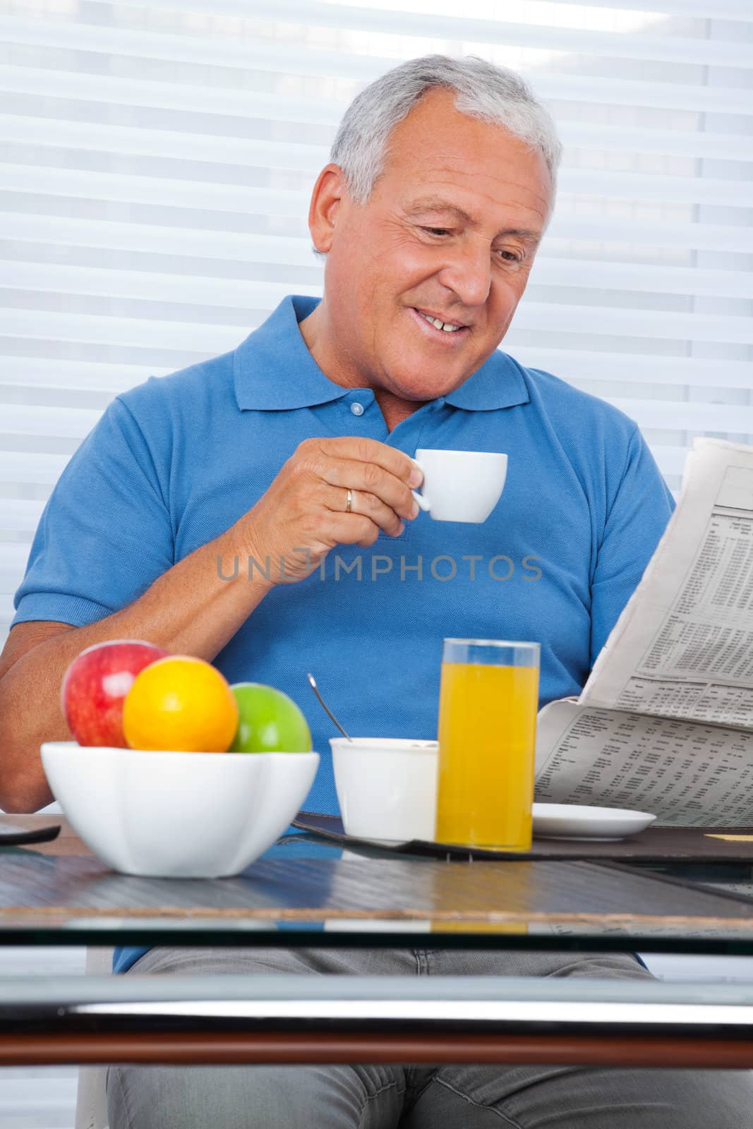 Smiling senior man reading newspaper while having breakfast at home