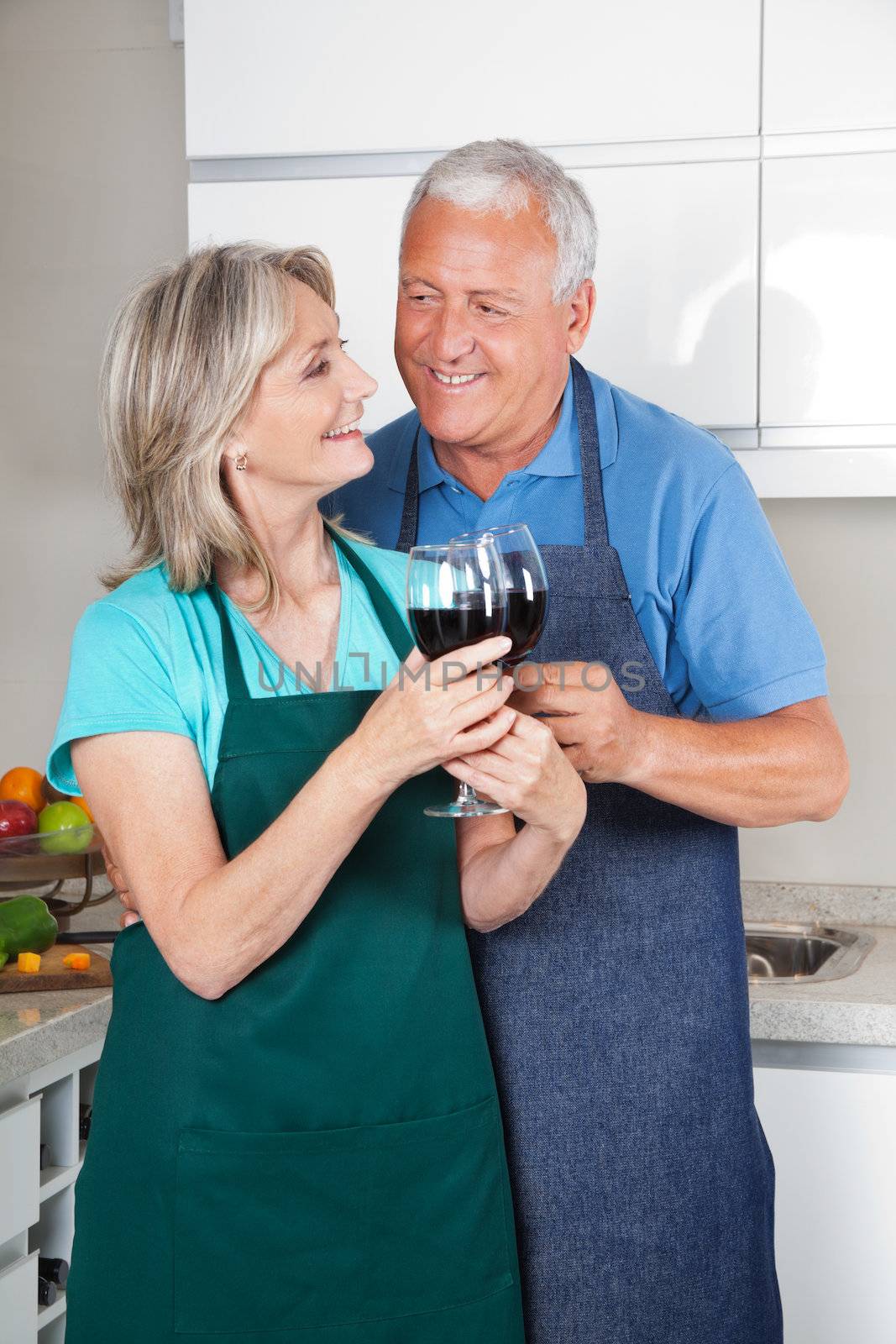Happy senior couple toasting wine glasses in the kitchen