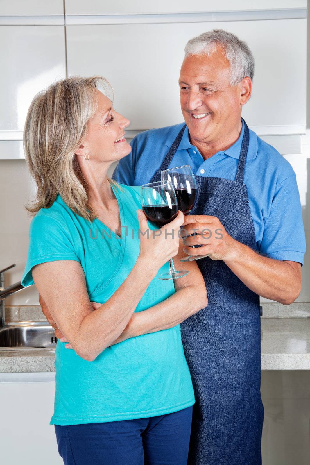 Happy senior couple toasting wine glasses in the kitchen