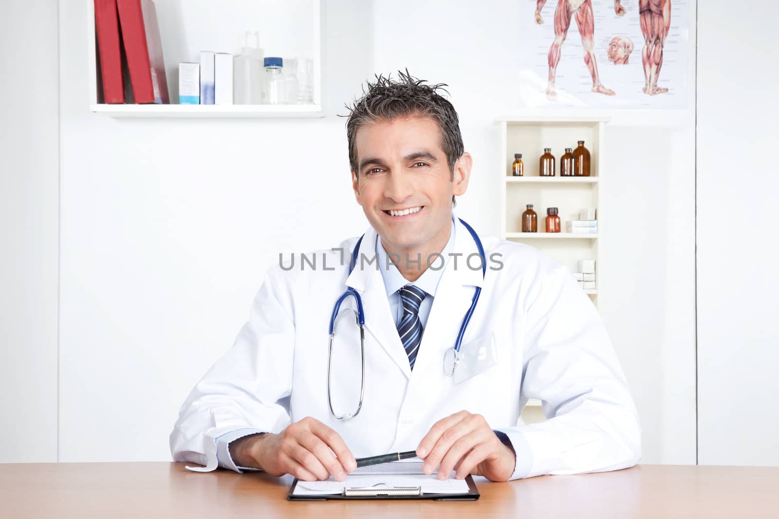 Male doctor sitting at desk with clipboard and pen.