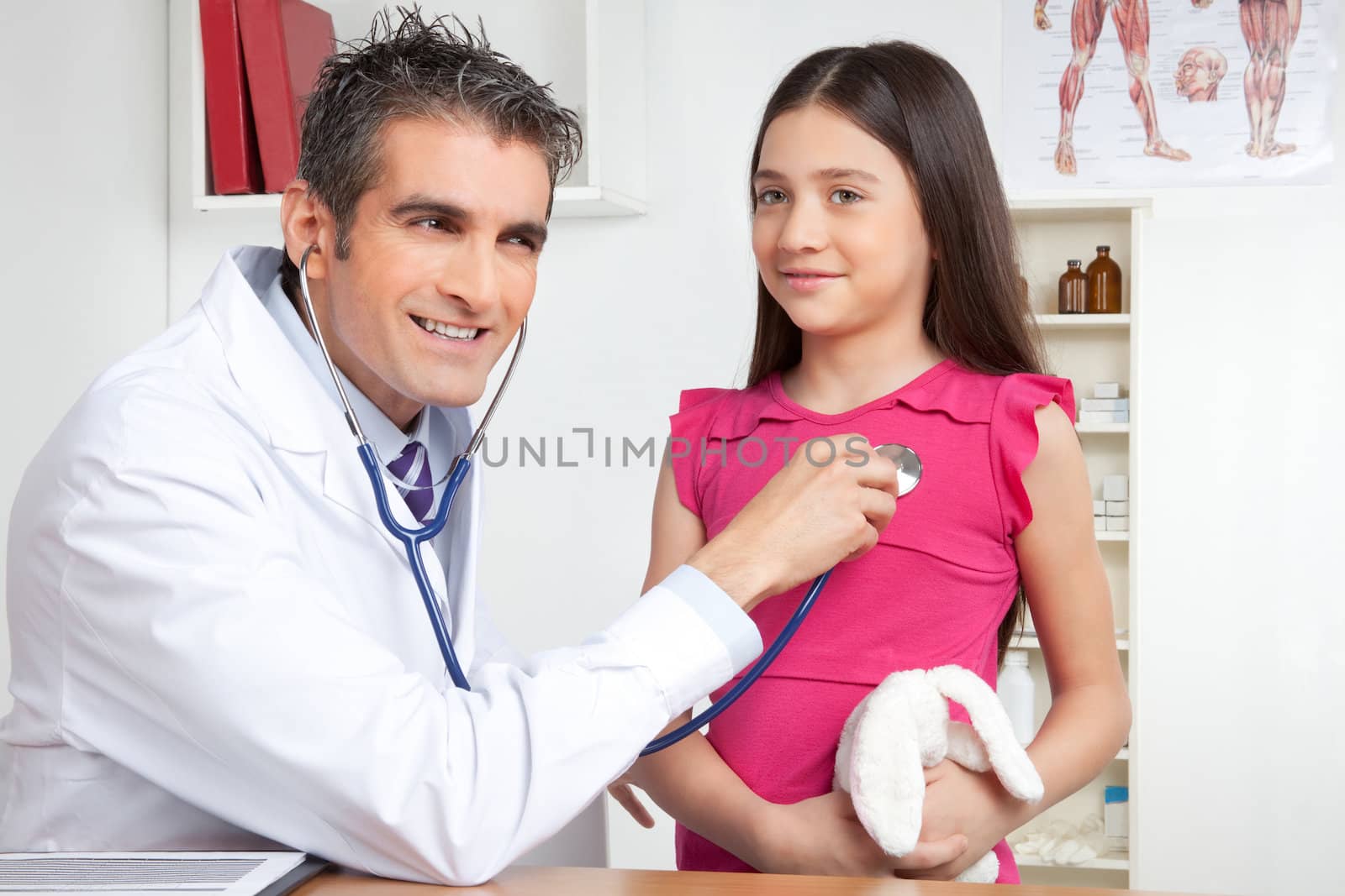 Happy male doctor examining child patient in clinic.