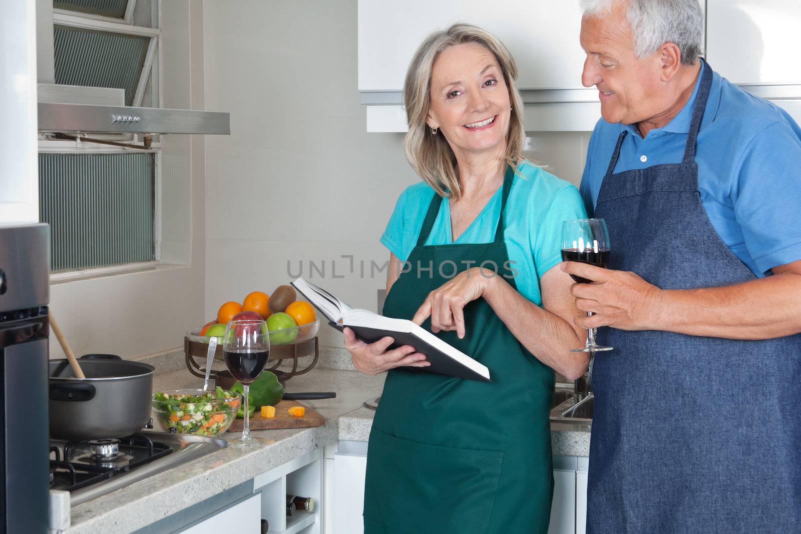 Portrait of smiling woman with recipe book and man holding wine glass in kitchen