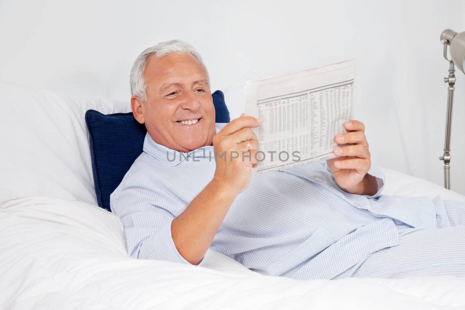 Relaxed senior man reading newspaper while lying on bed at home
