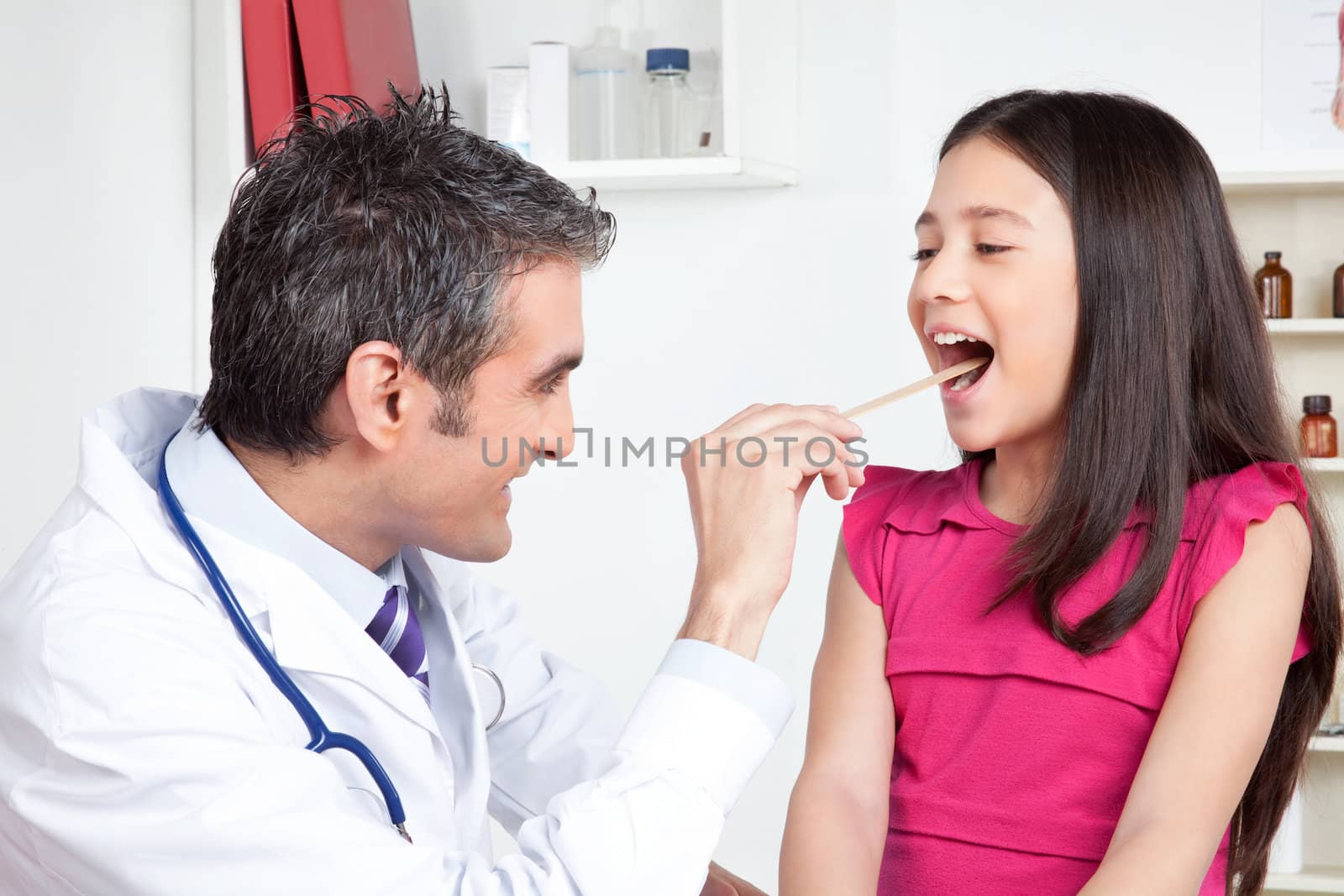 Happy male doctor examining child mouth in clinic.