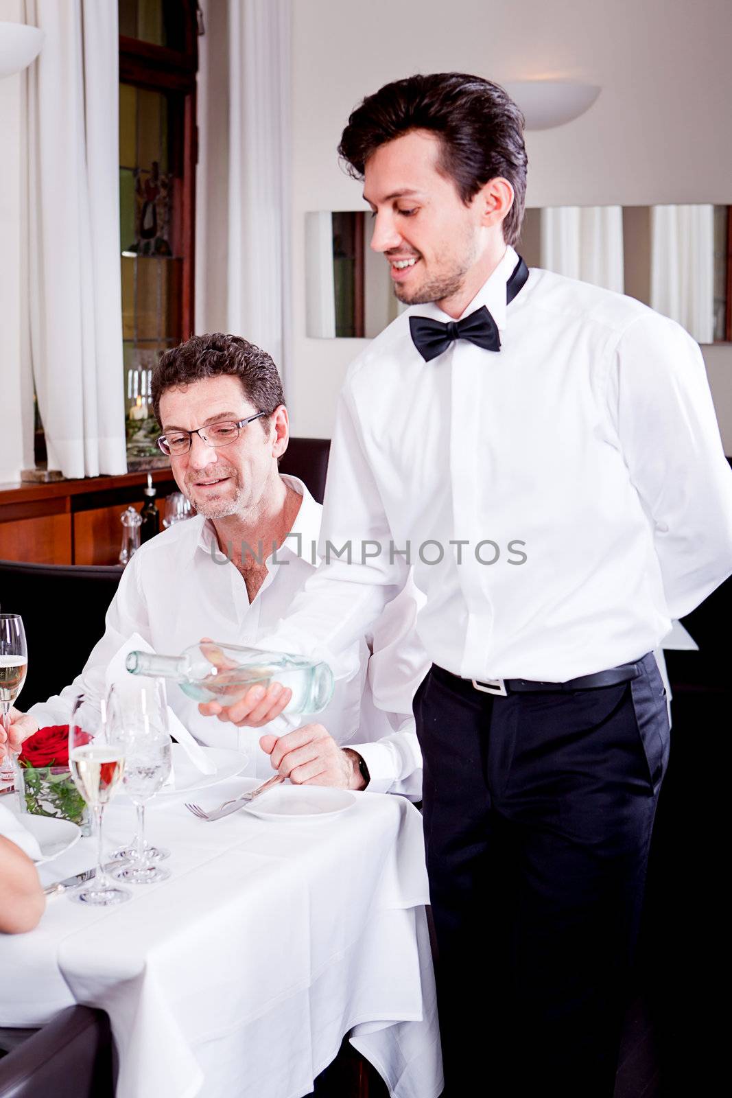 man and woman for dinner in restaurant waiter serving mineral water 