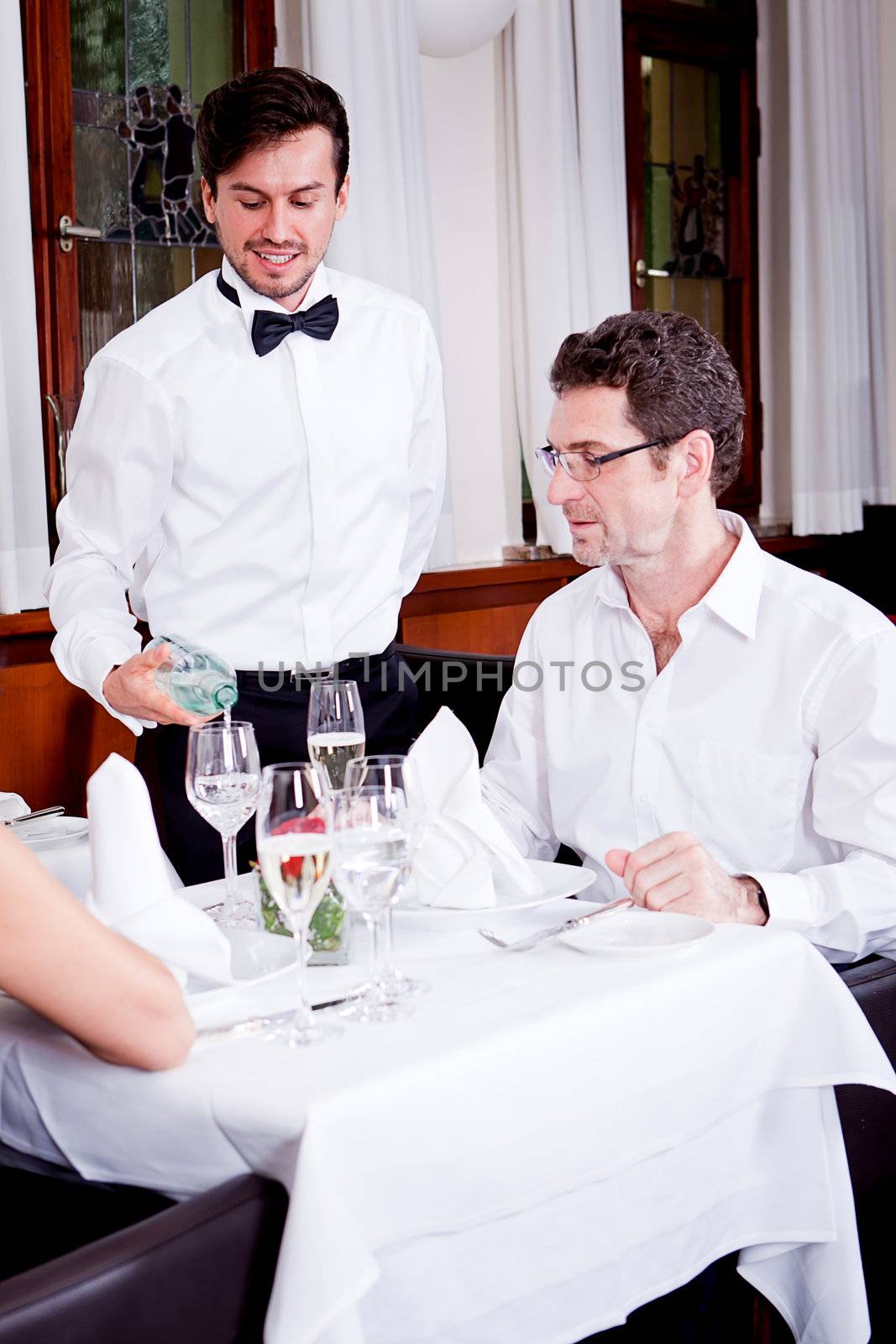 man and woman for dinner in restaurant waiter serving mineral water 