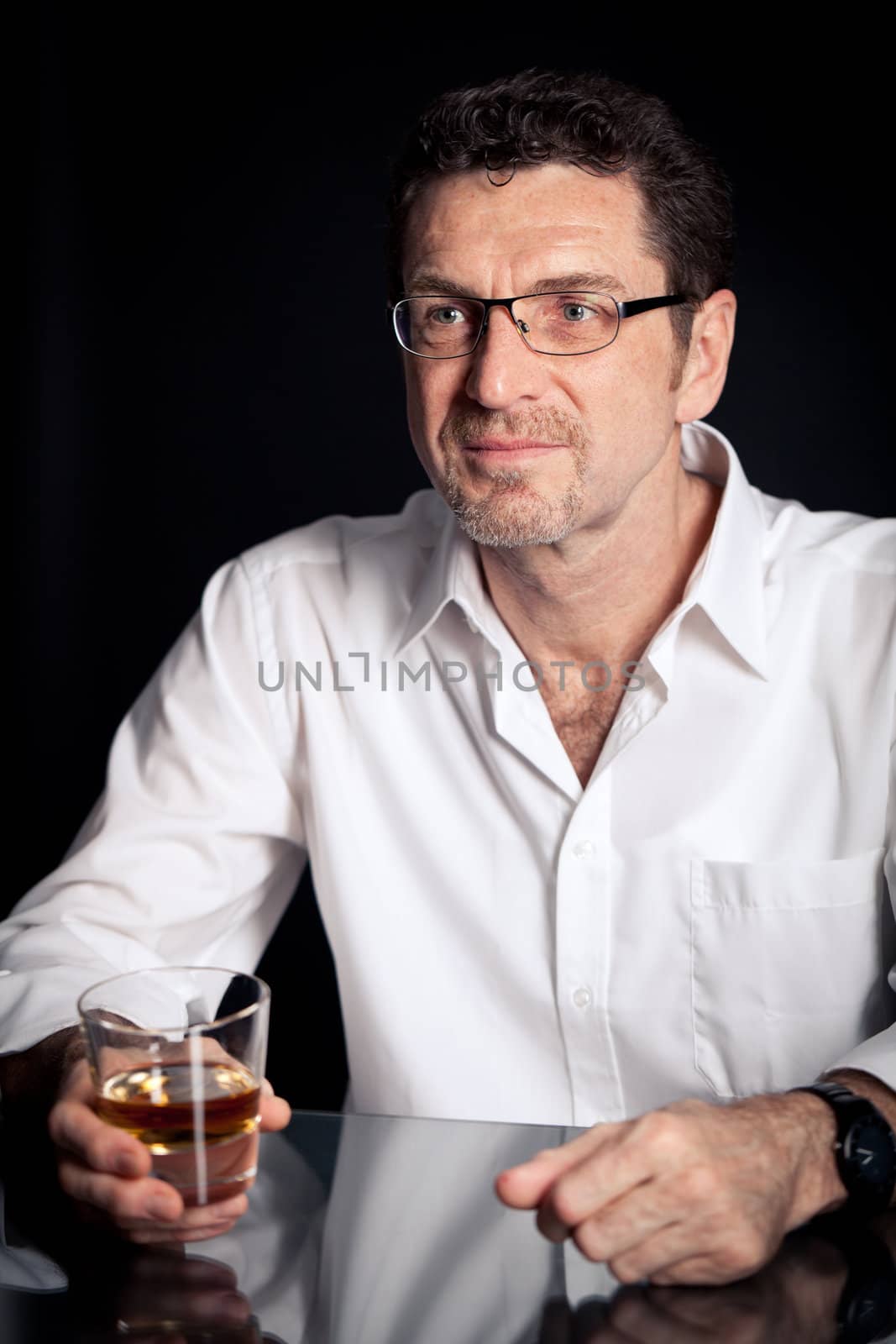 adult man holding an alcoholic drink thoughtful on black background
