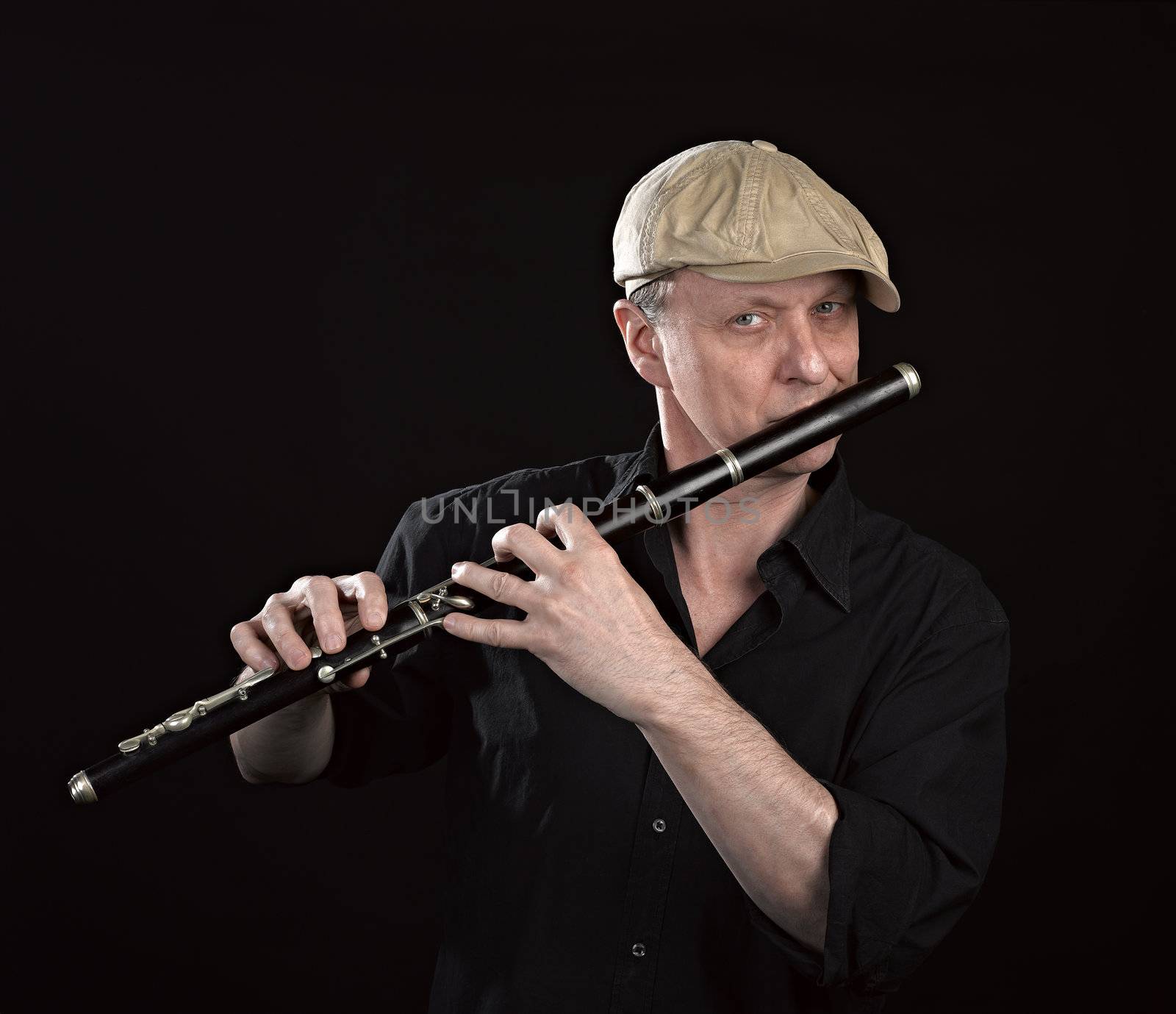 Portrait of a man playing ols wooden transverse flute, isolated on black