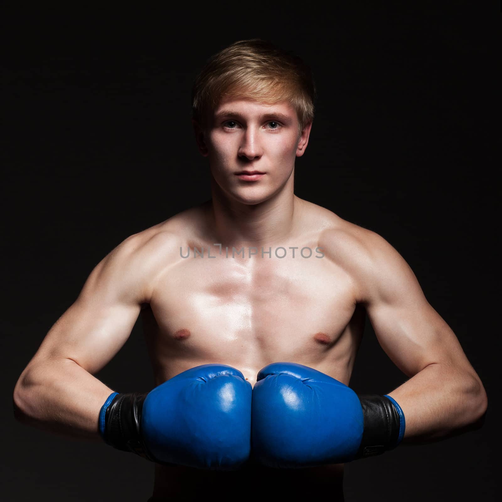 Young handsome boxer in blue gloves over dark background