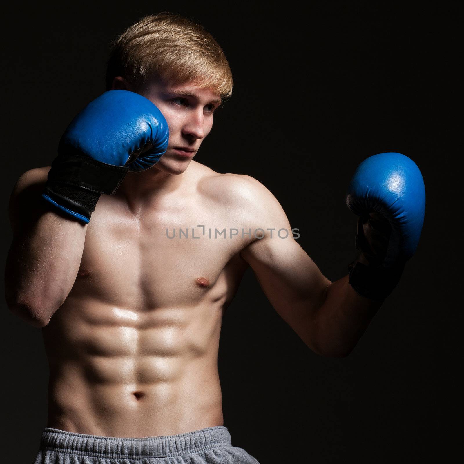 Young handsome boxer in a movement over dark background