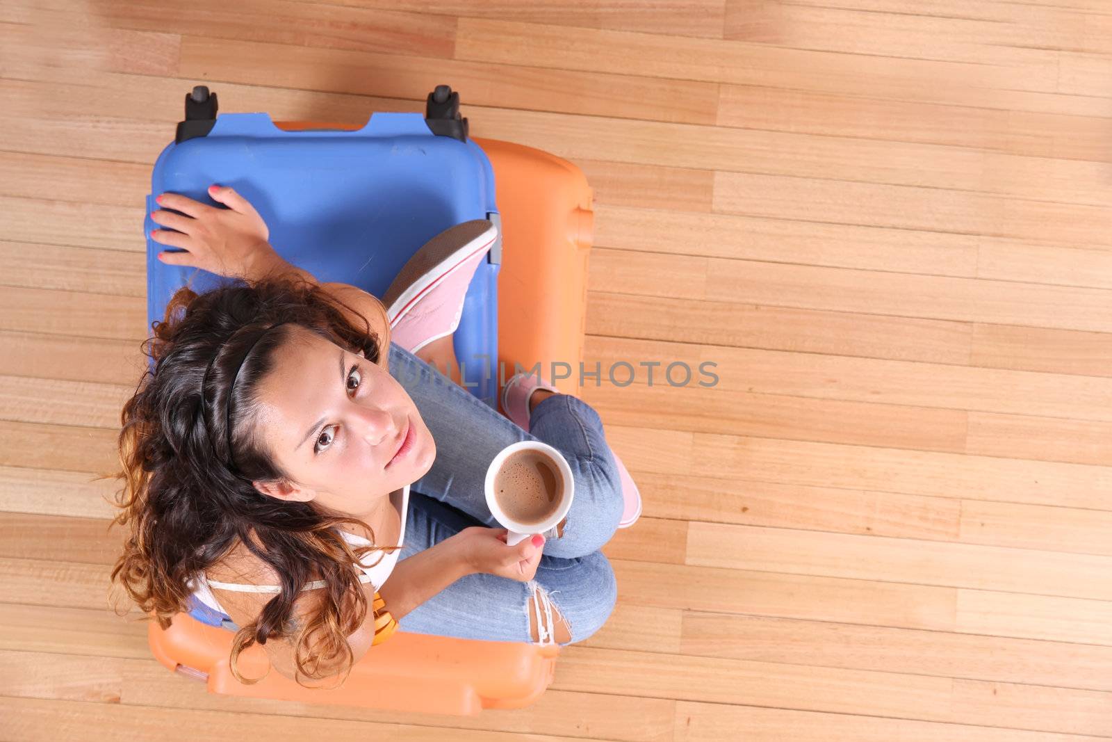 A young woman sitting on a stack of suitcases while drinking coffee and waiting for the departure to vacations.