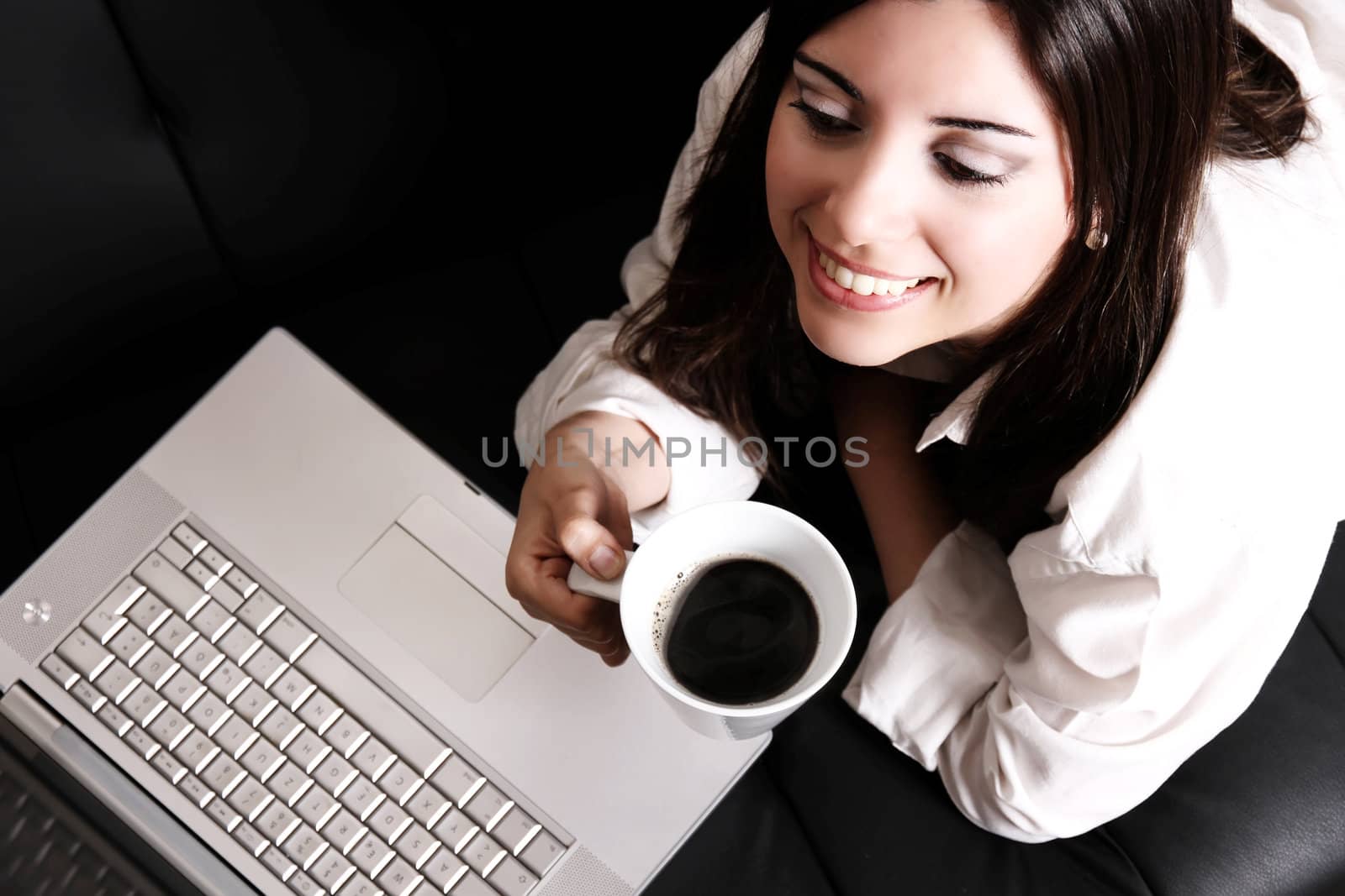 A young, hispanic adult girl watching a Laptop while drinking coffee.