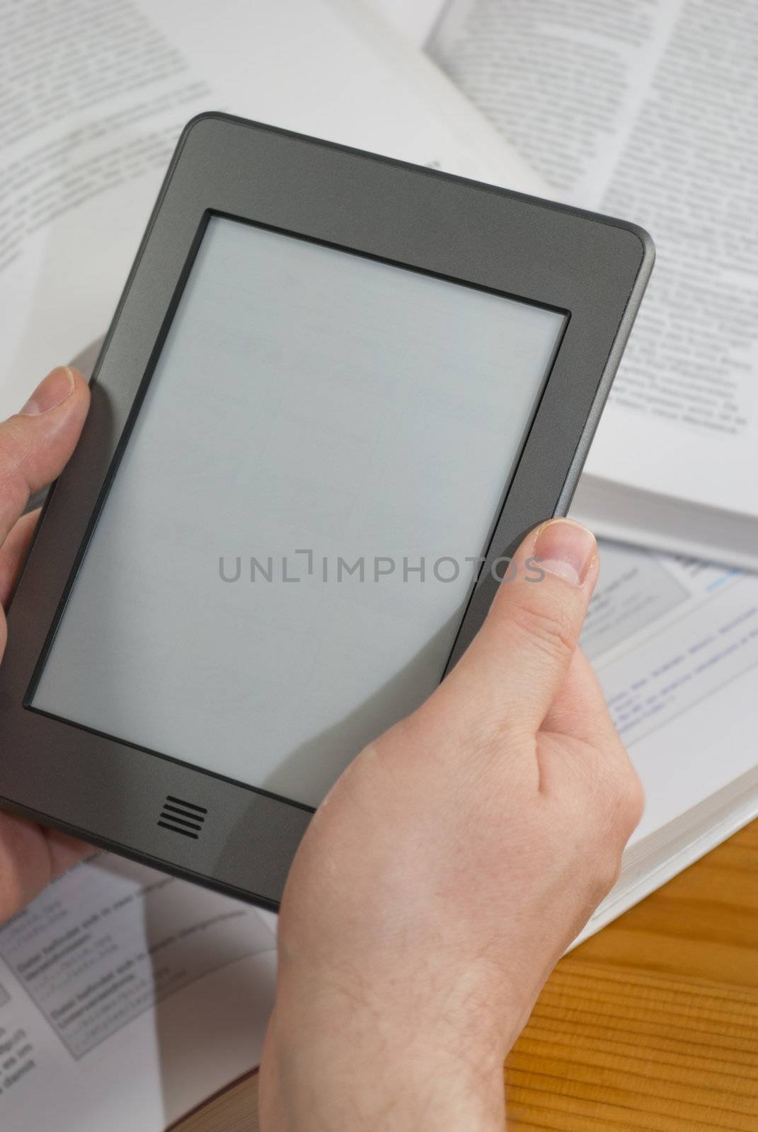 Man's hands holding  an electronic book reader with blank screen, open books in the background