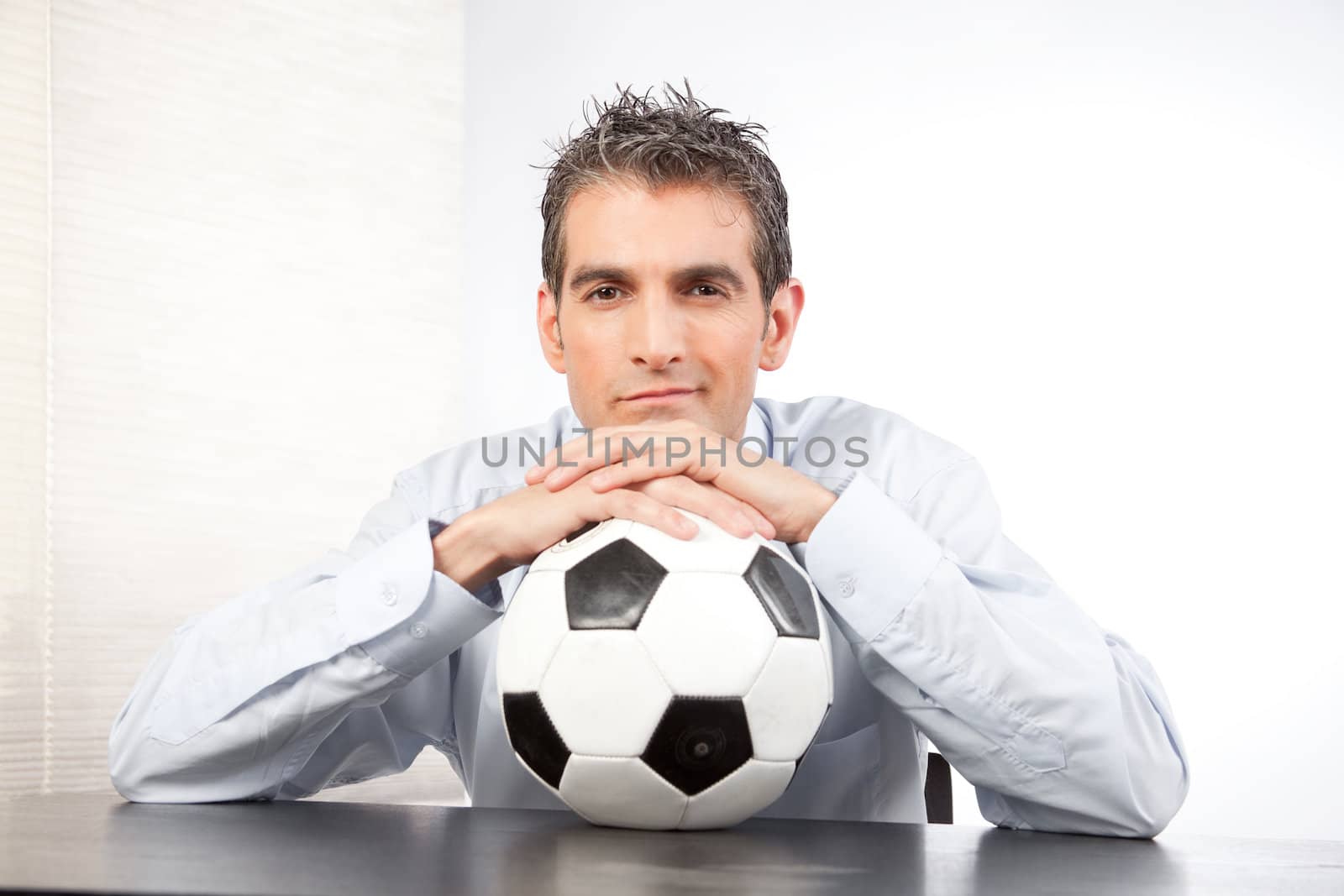 Businessman with football sitting at desk .