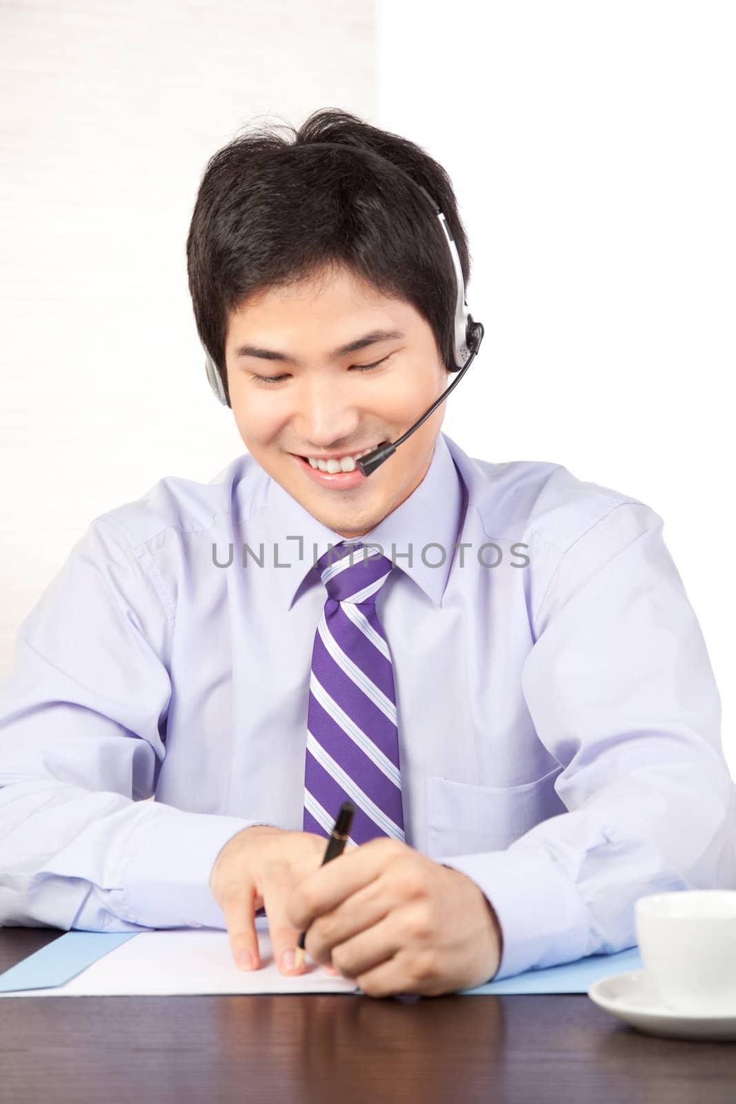 Asian businessman wearing a headset sitting at desk isolated on white background.