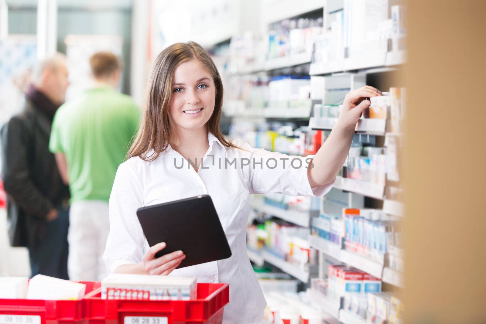 Portrait of female pharmacist holding tablet PC standing by the shelf at drugstore