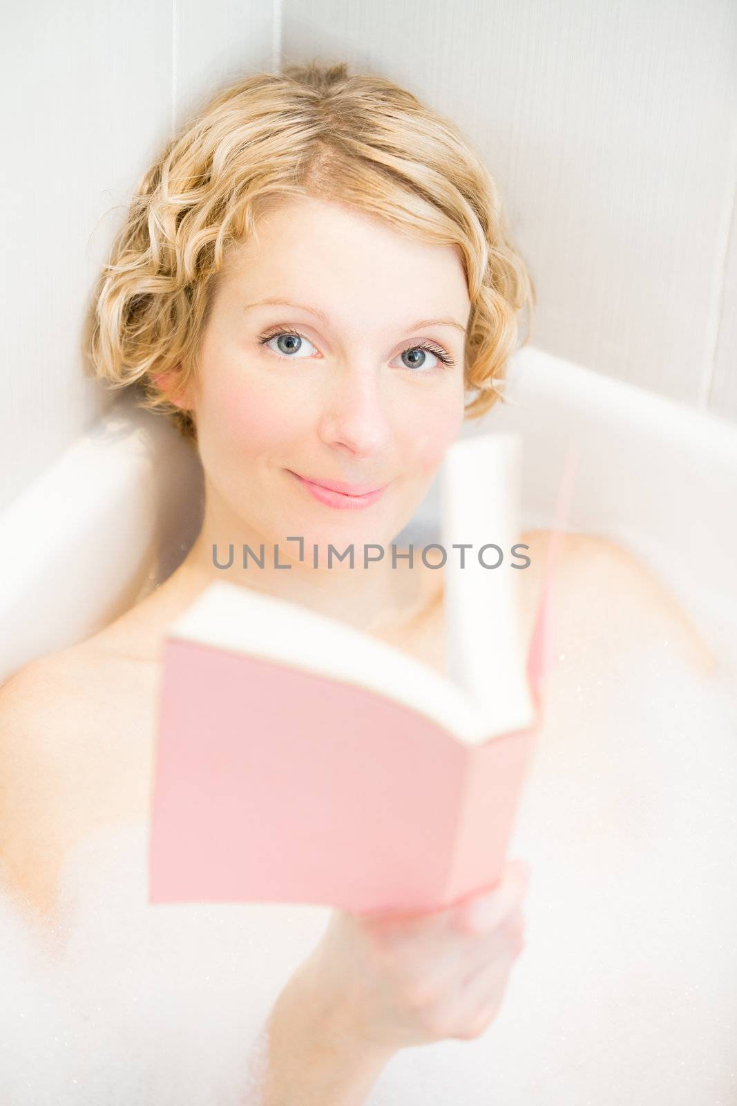 Hayy young woman relaxing and reading a book in the bath