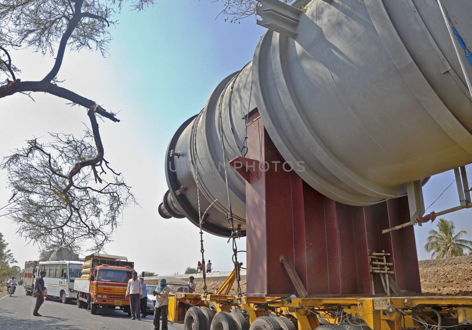 A heavy goods transporter has his cargo stuck between two trees on either side of a tree lined road and road crew and emergency services clearing the accident and traffic jam on 25th February 2013, horizontal landscape caught on the coastal road in Gujarat India, between Bhavnagar and Mangrol.