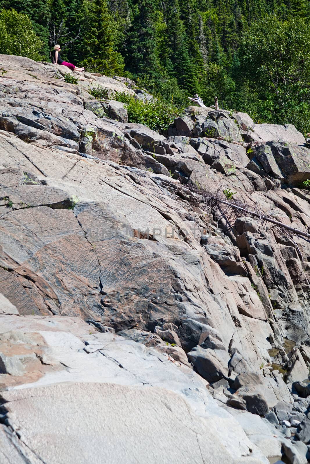 Girl sitting very far on a huge rock