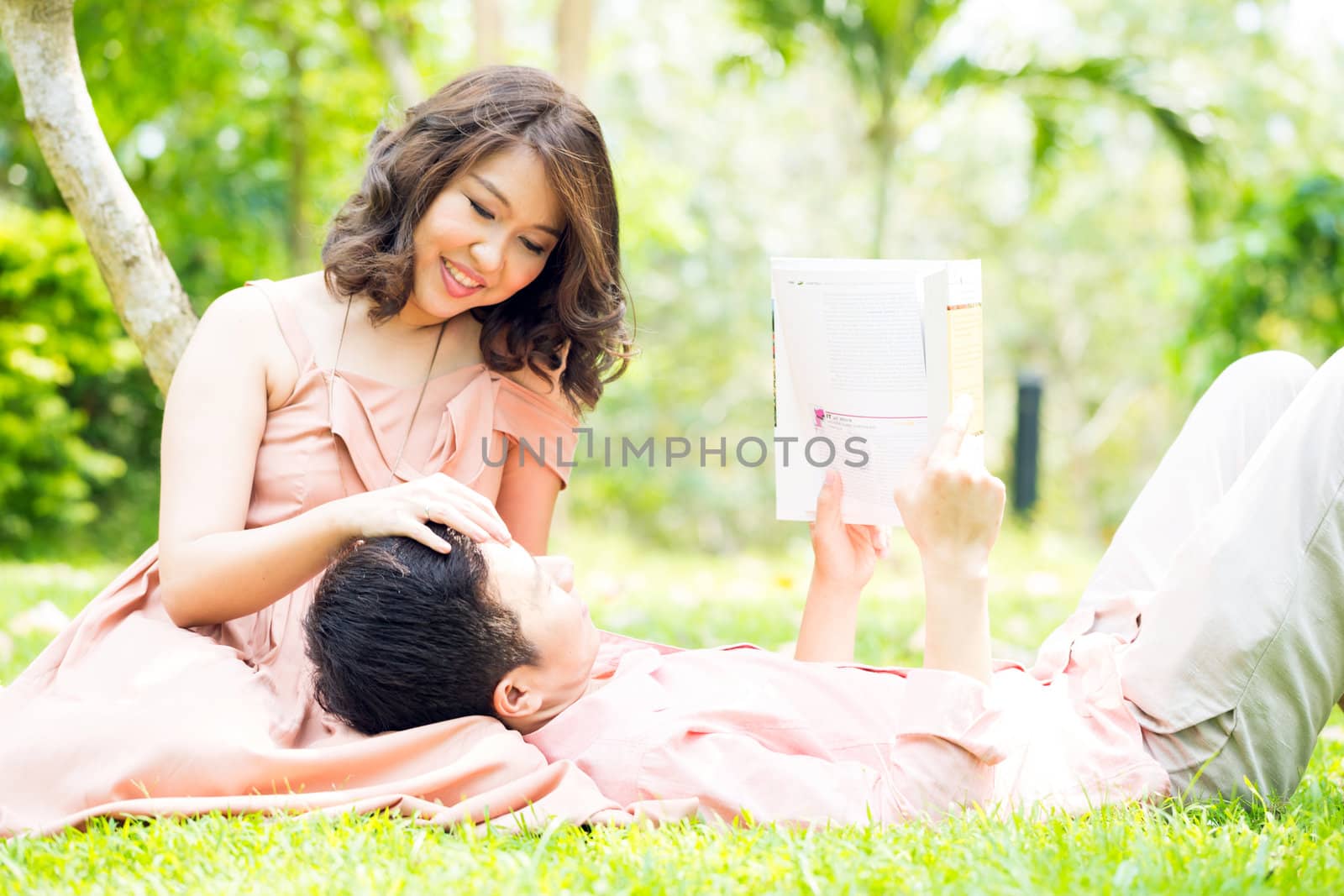 Couple relaxing in the garden, young man reading a book and lying on his girlfriend lap