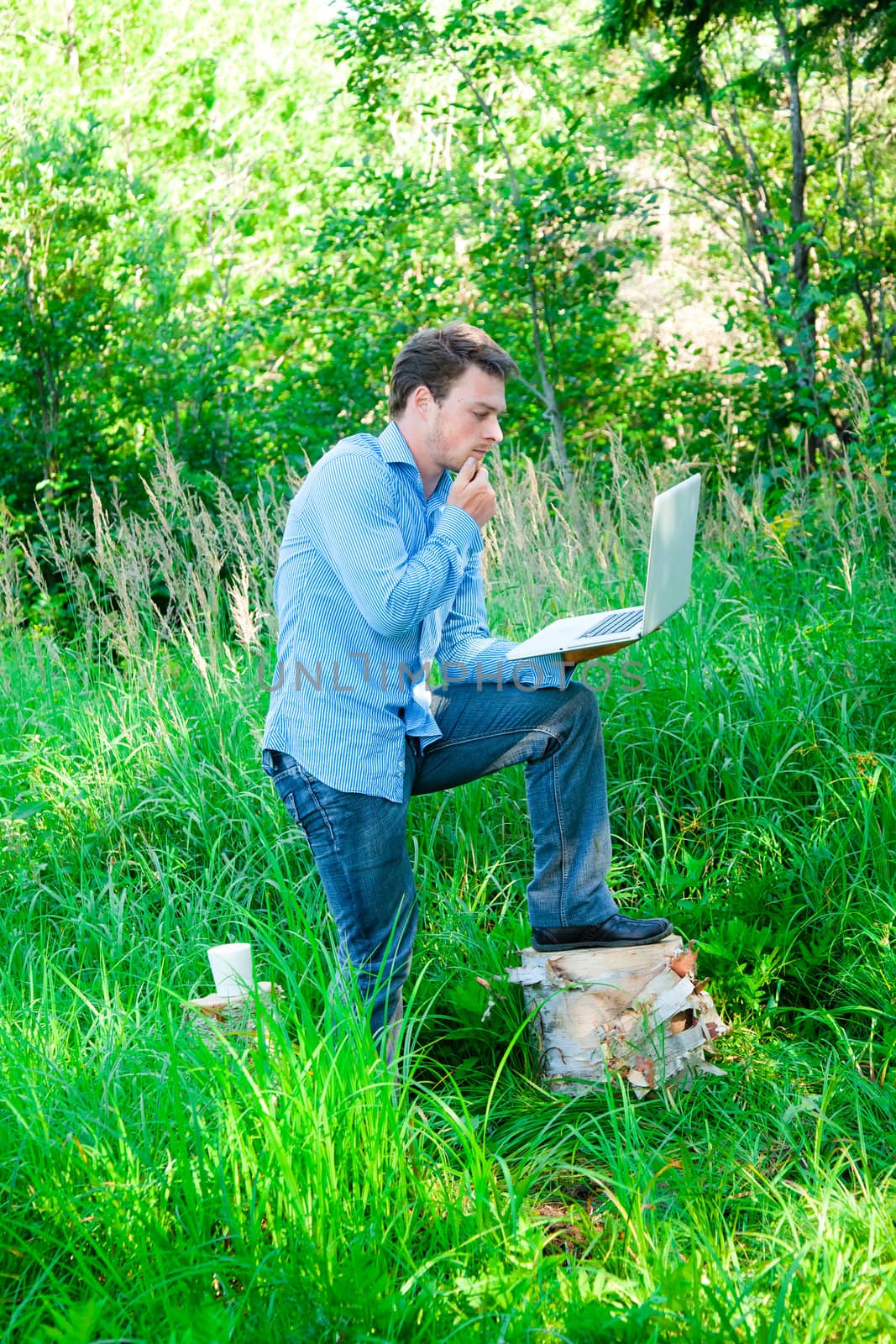 Pensive young man outdoors with a cup and laptop