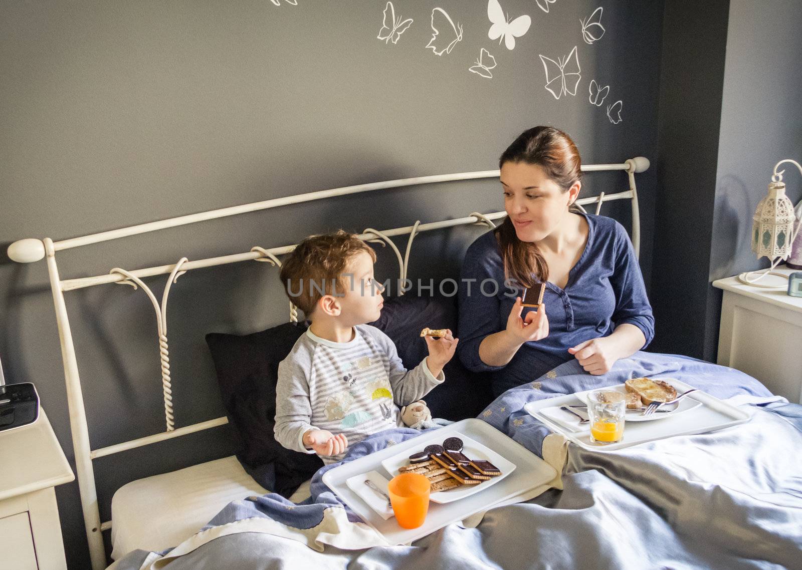 Happy mother and son having breakfast in bed at home in the morning