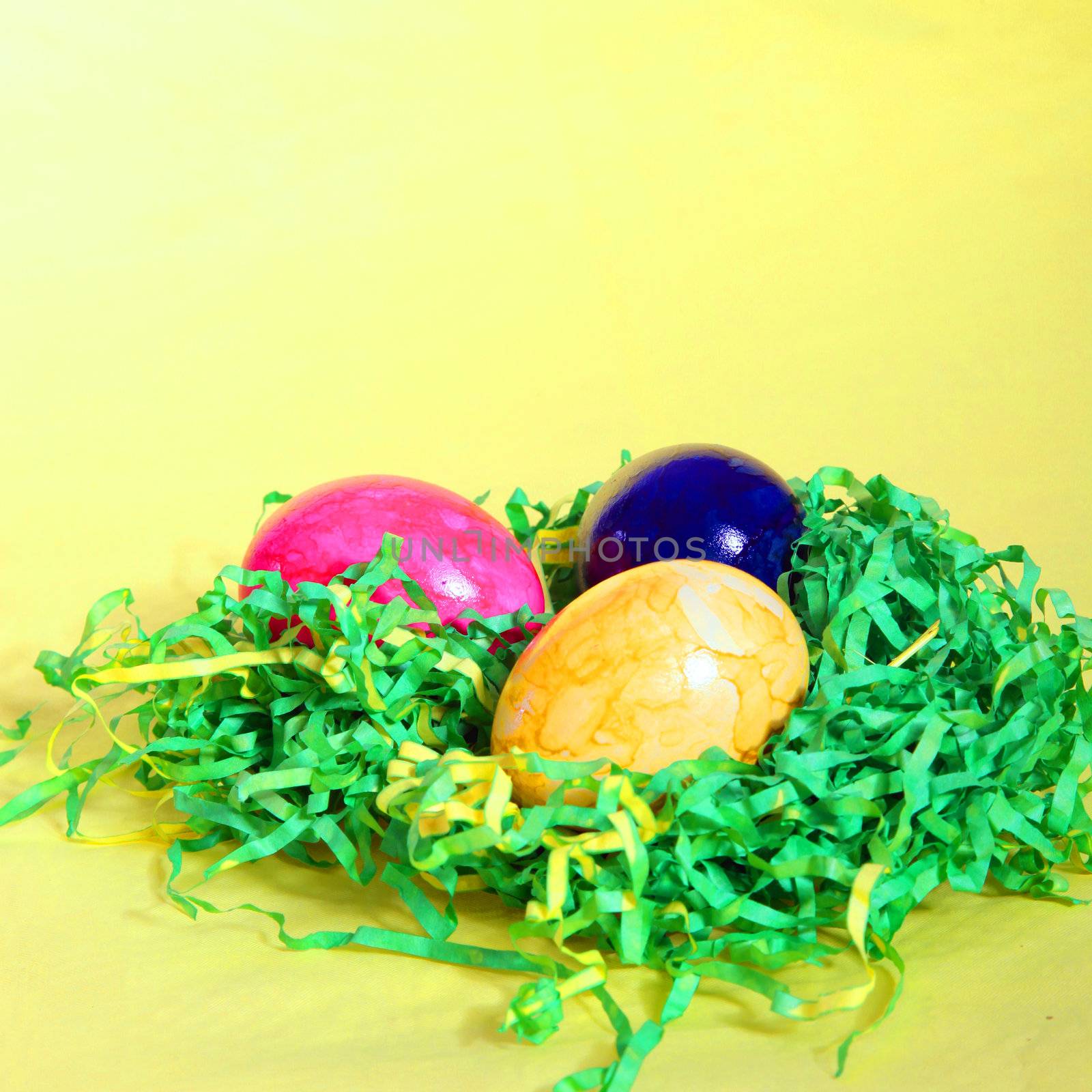 Colourful hand painted marbled Easter Eggs on a bed of artificial green straw against a yellow background with copyspace