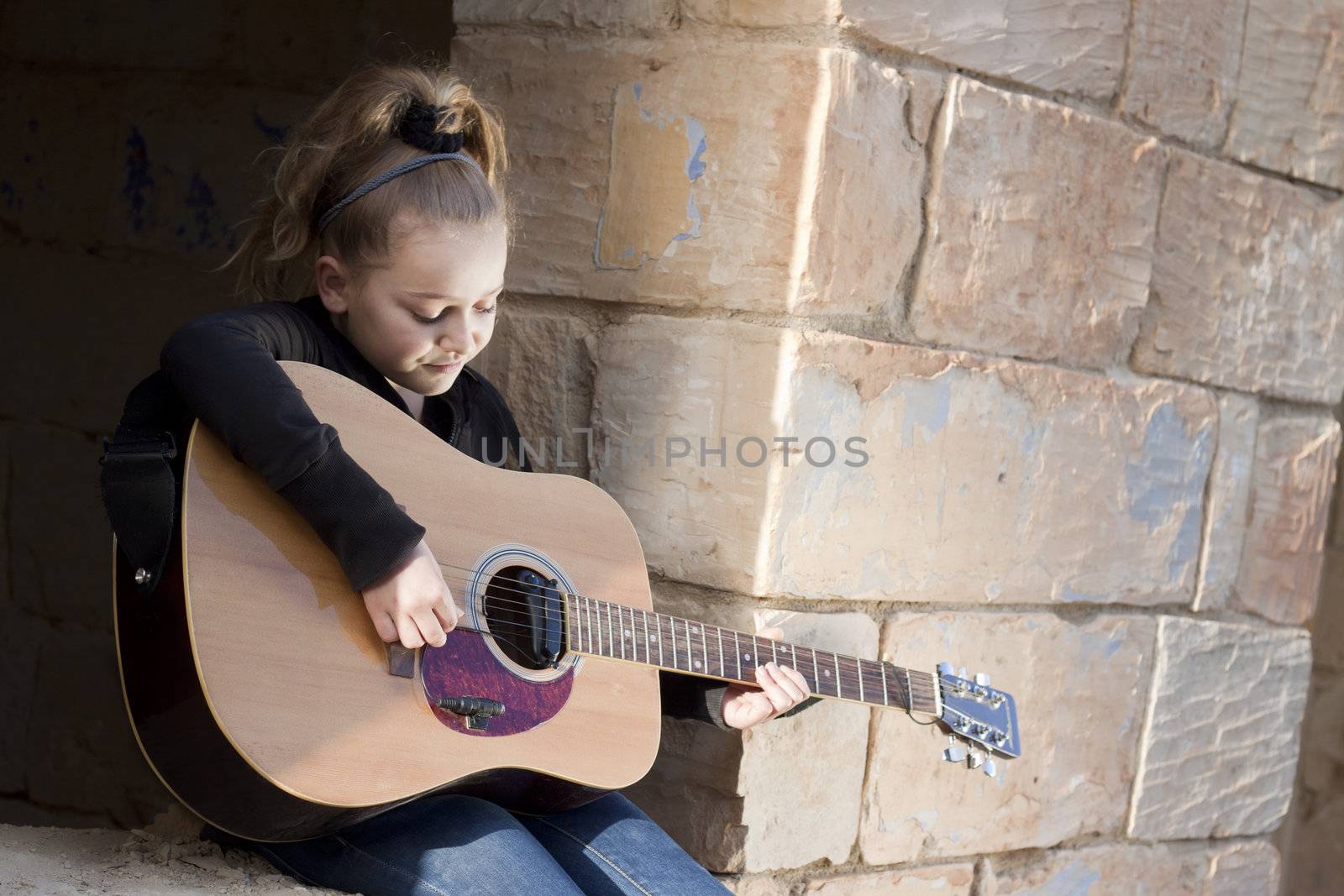 A girl learning or practicing on a musical instrument, a guitar. Space for text