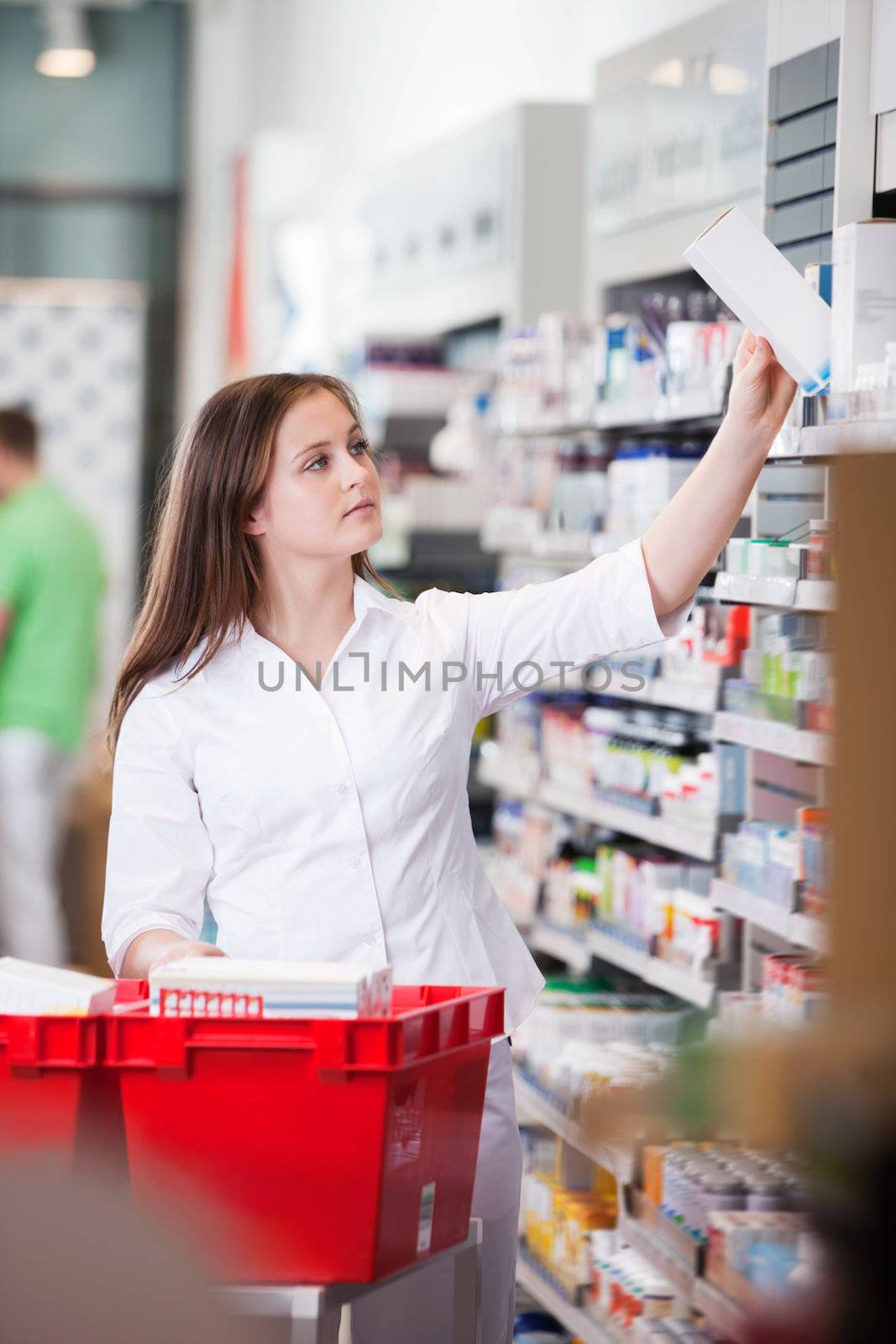 Female pharmacist keeping medicine box on the shelf at drugstore