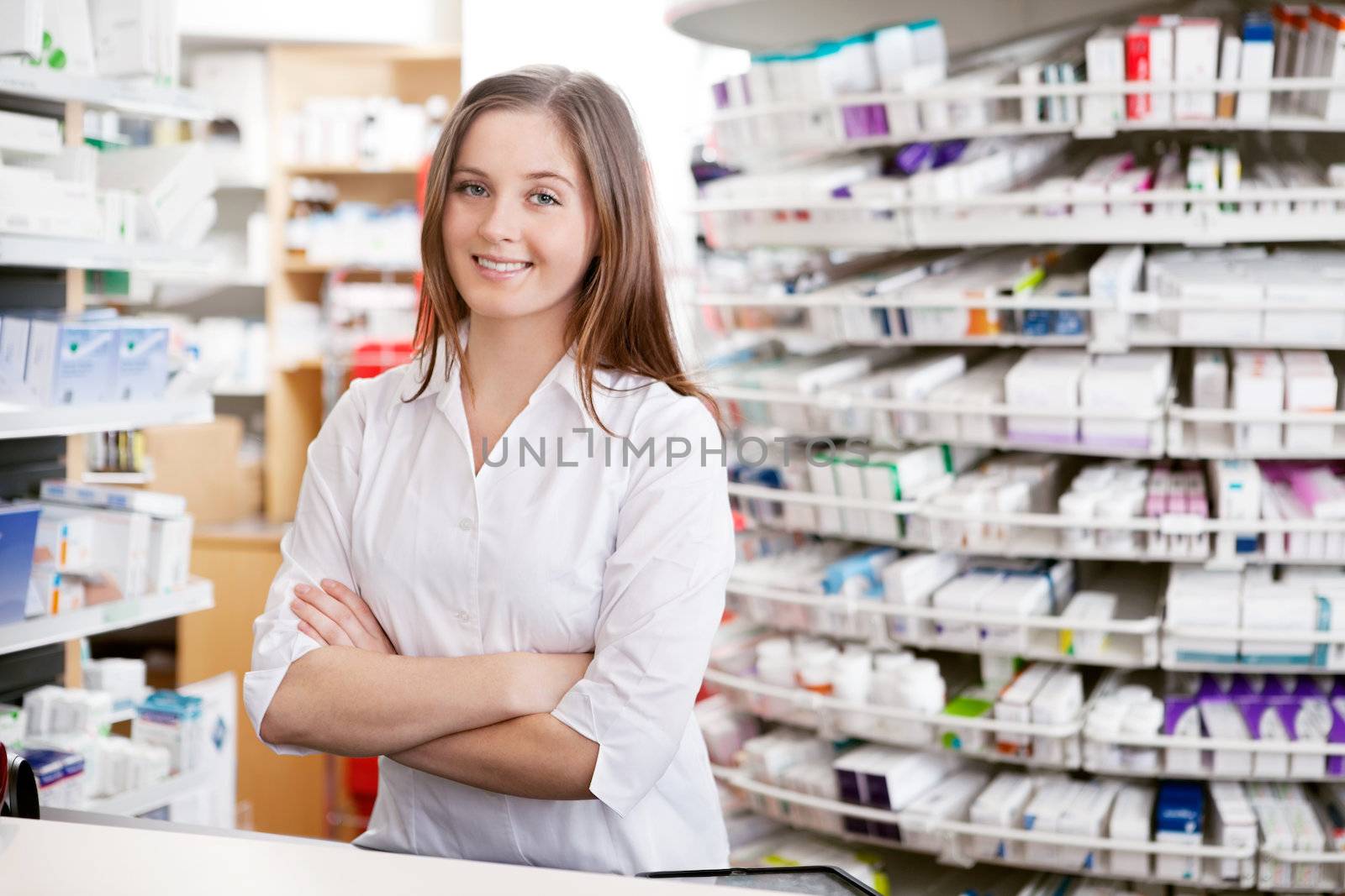 Portrait of female pharmacist standing with arms crossed at counter in pharmacy