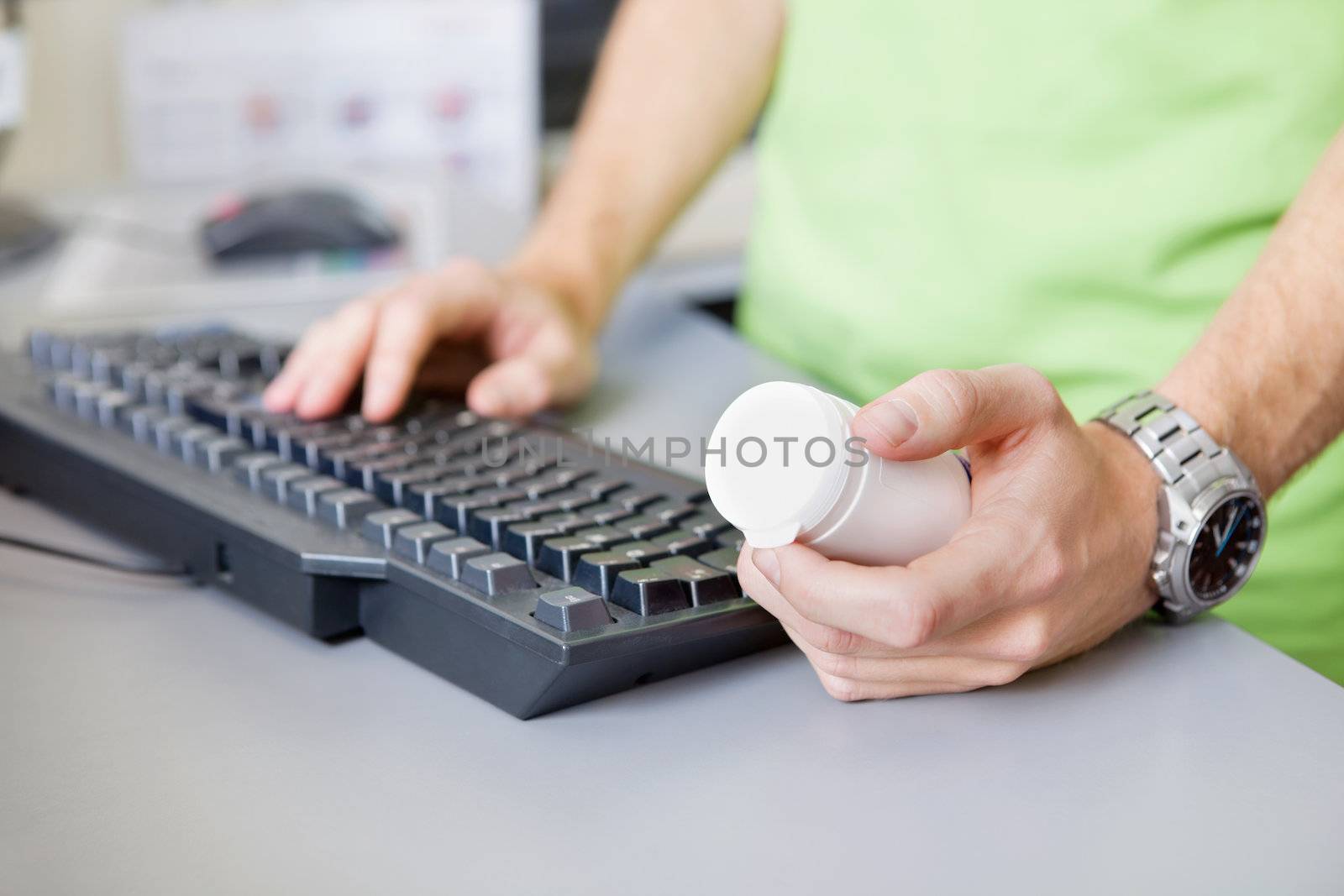 Cropped image of male hand holding medicine container while typing on keyboard