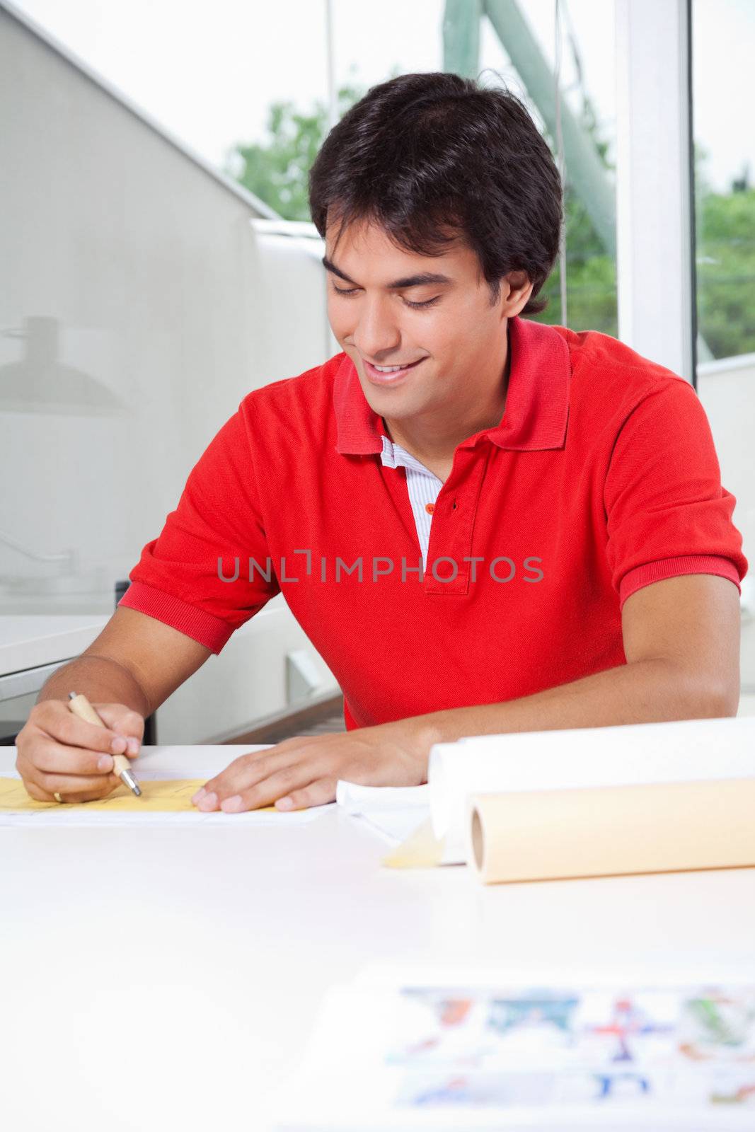 Young male architect in casual t-shirt working on blueprint while sitting at home