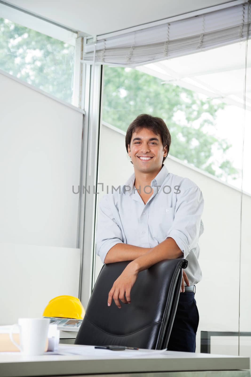 Portrait of happy young male architect standing by office chair