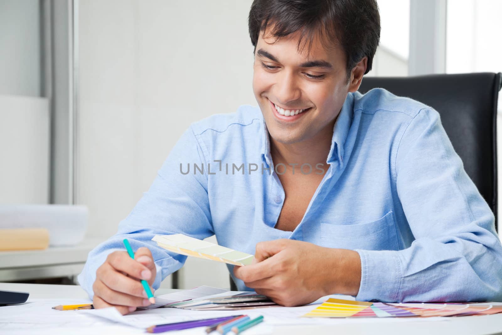 Happy young male interior designer looking at color swatches