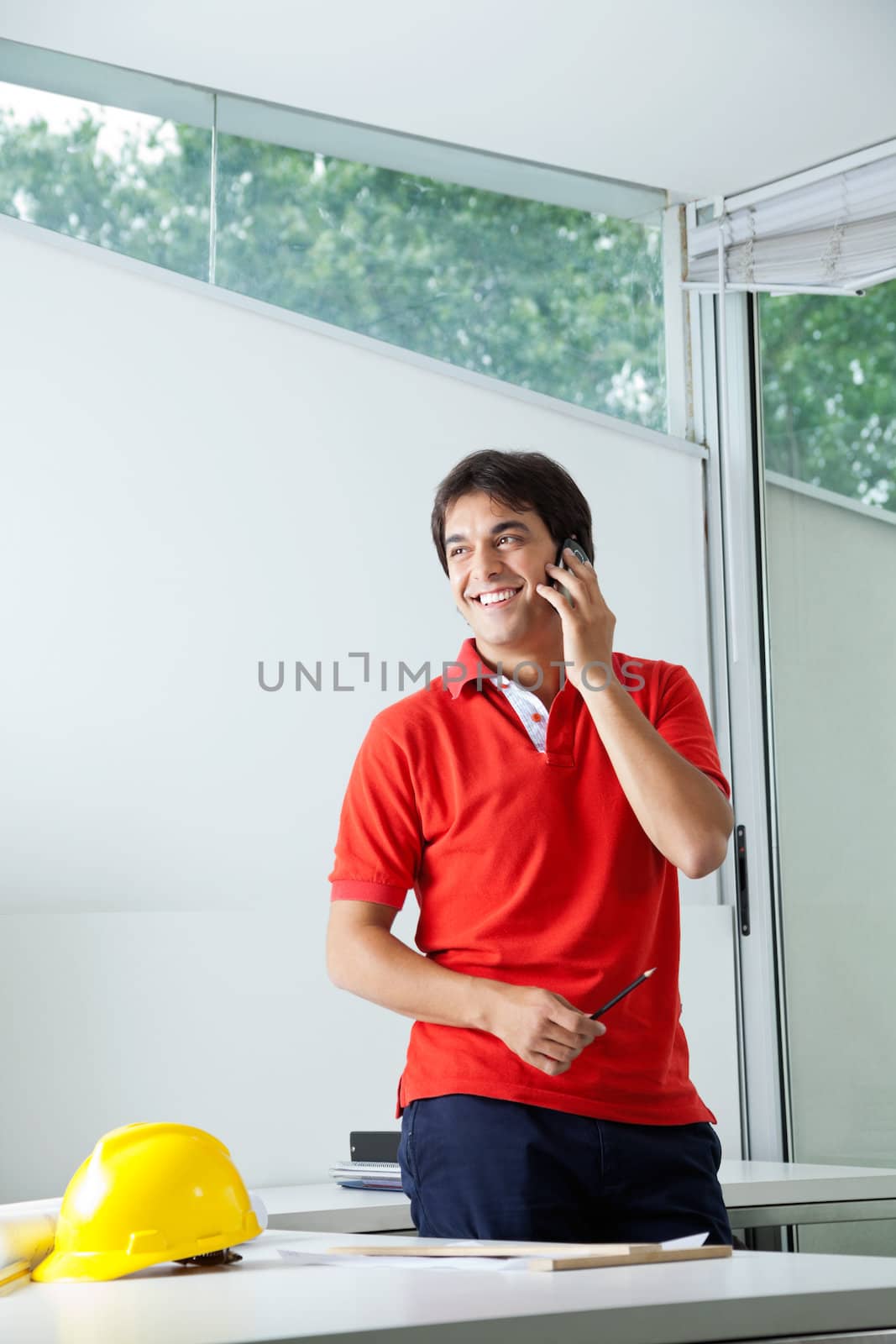 Young male architect smiling while answering phone call