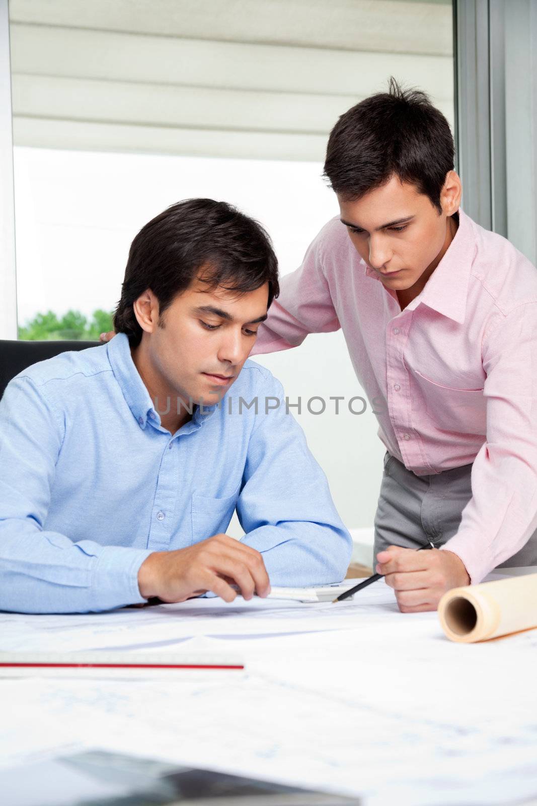 Young male architects working on blueprint together in office