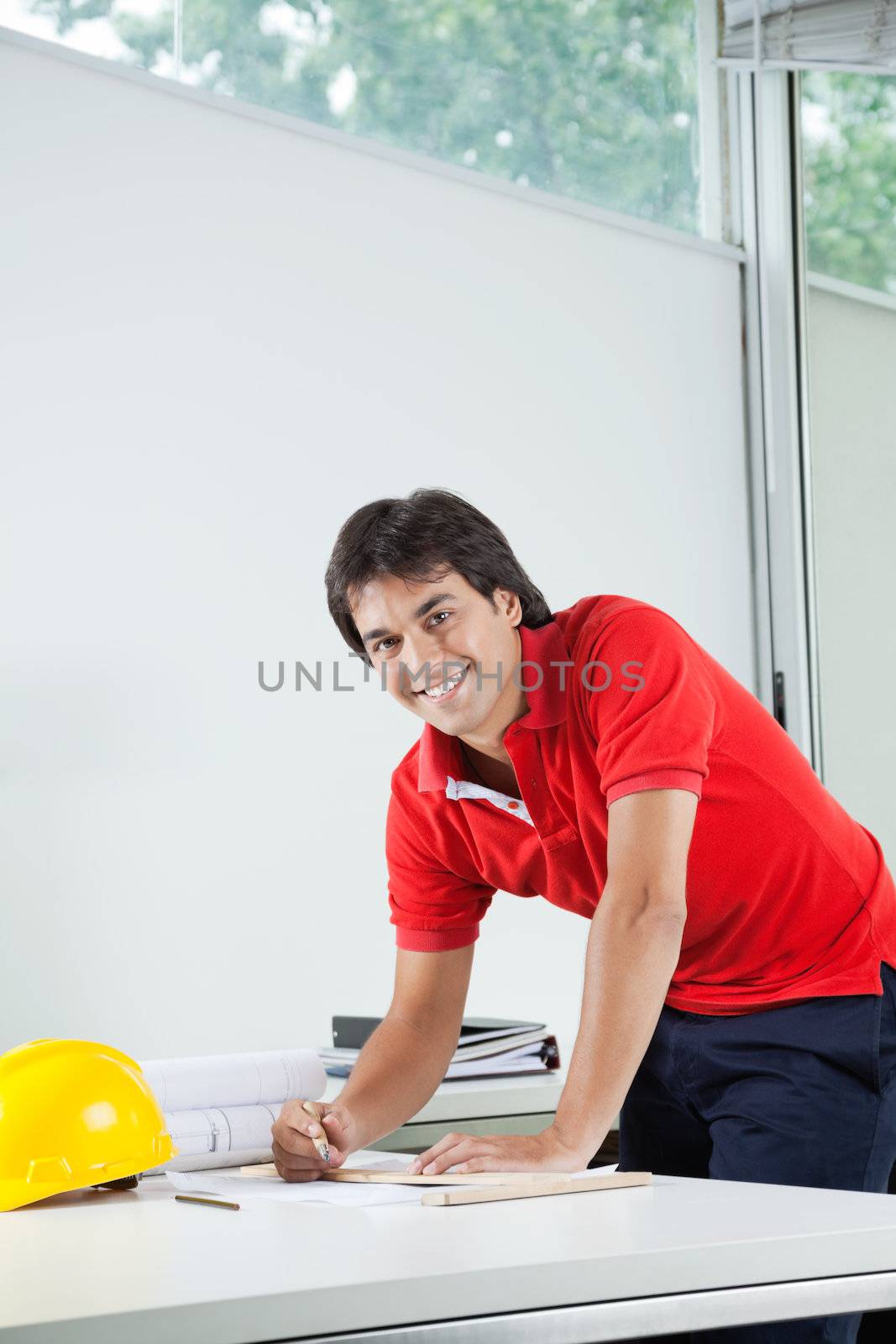 Portrait of young male architect smiling while working on blueprint