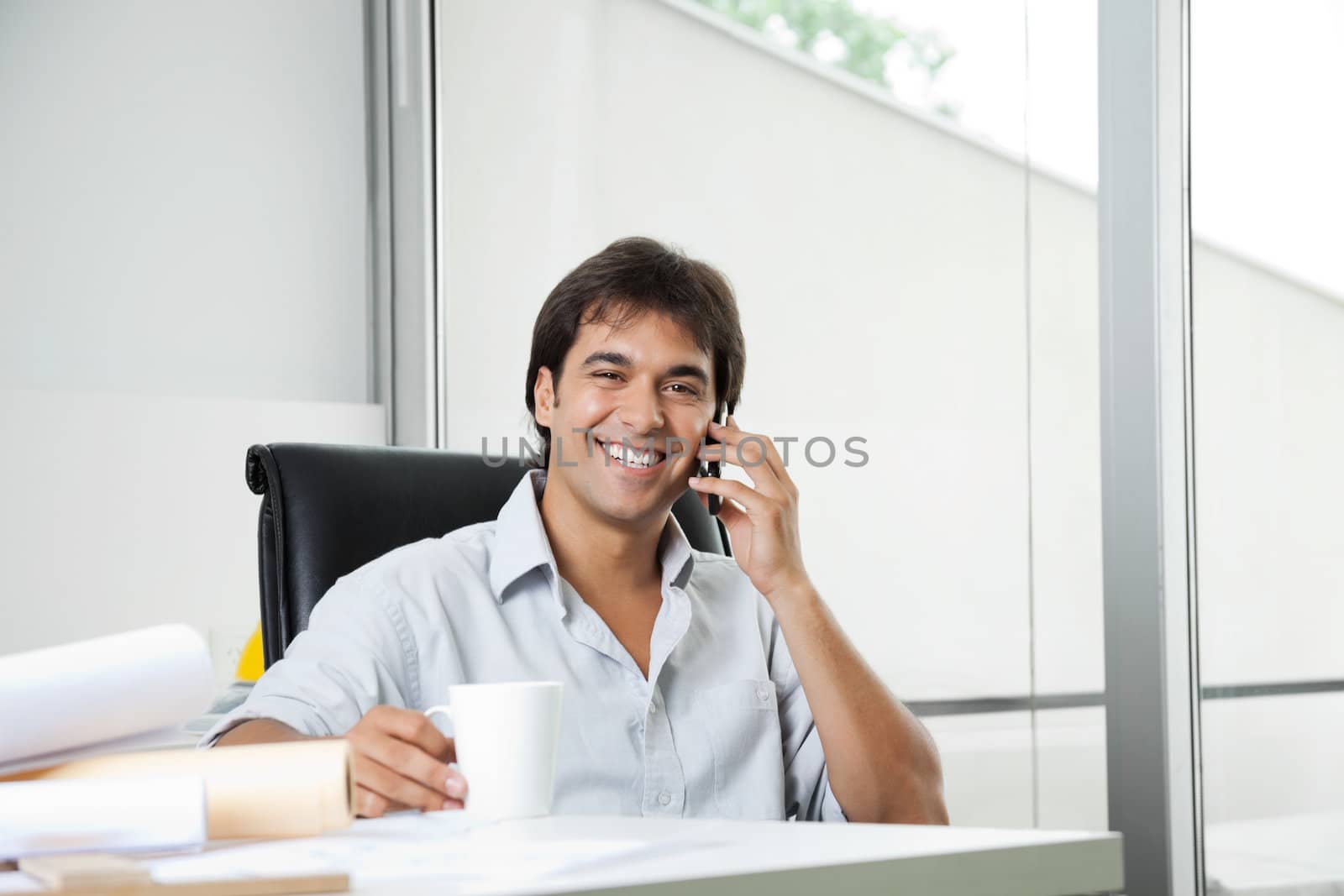 Portrait of cheerful young male architect answering phone call while having coffee
