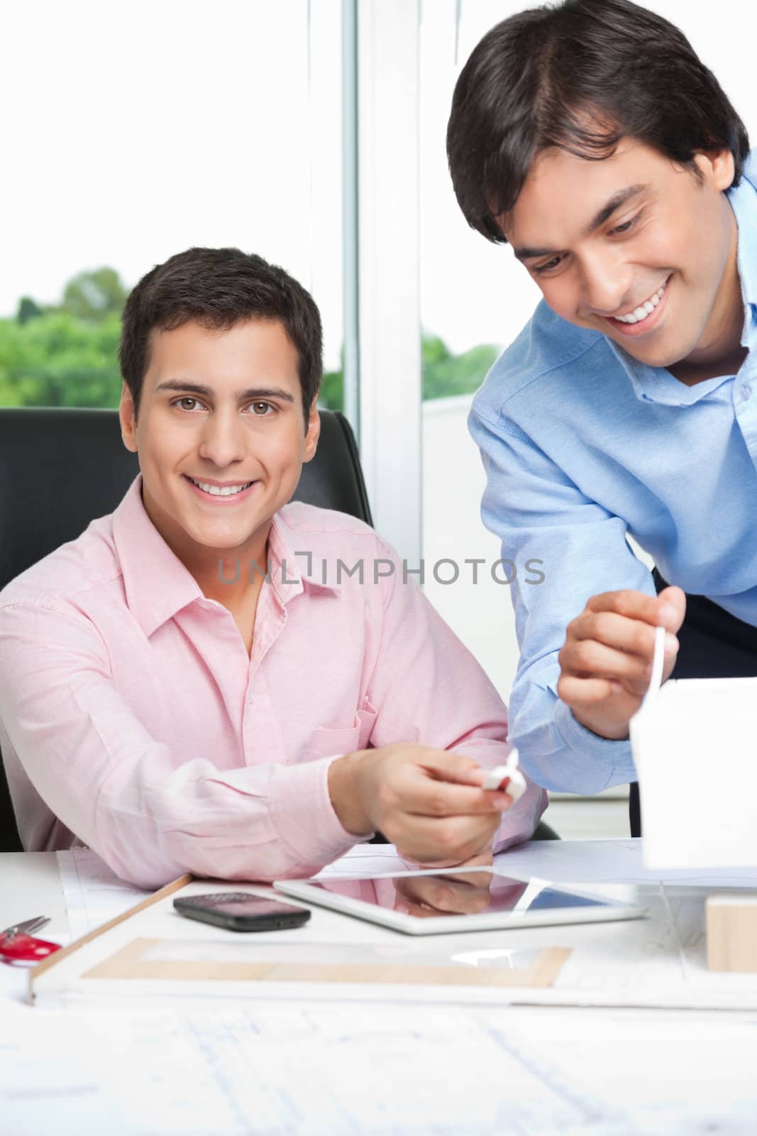 Portrait of happy young male architect at desk with colleague standing beside.