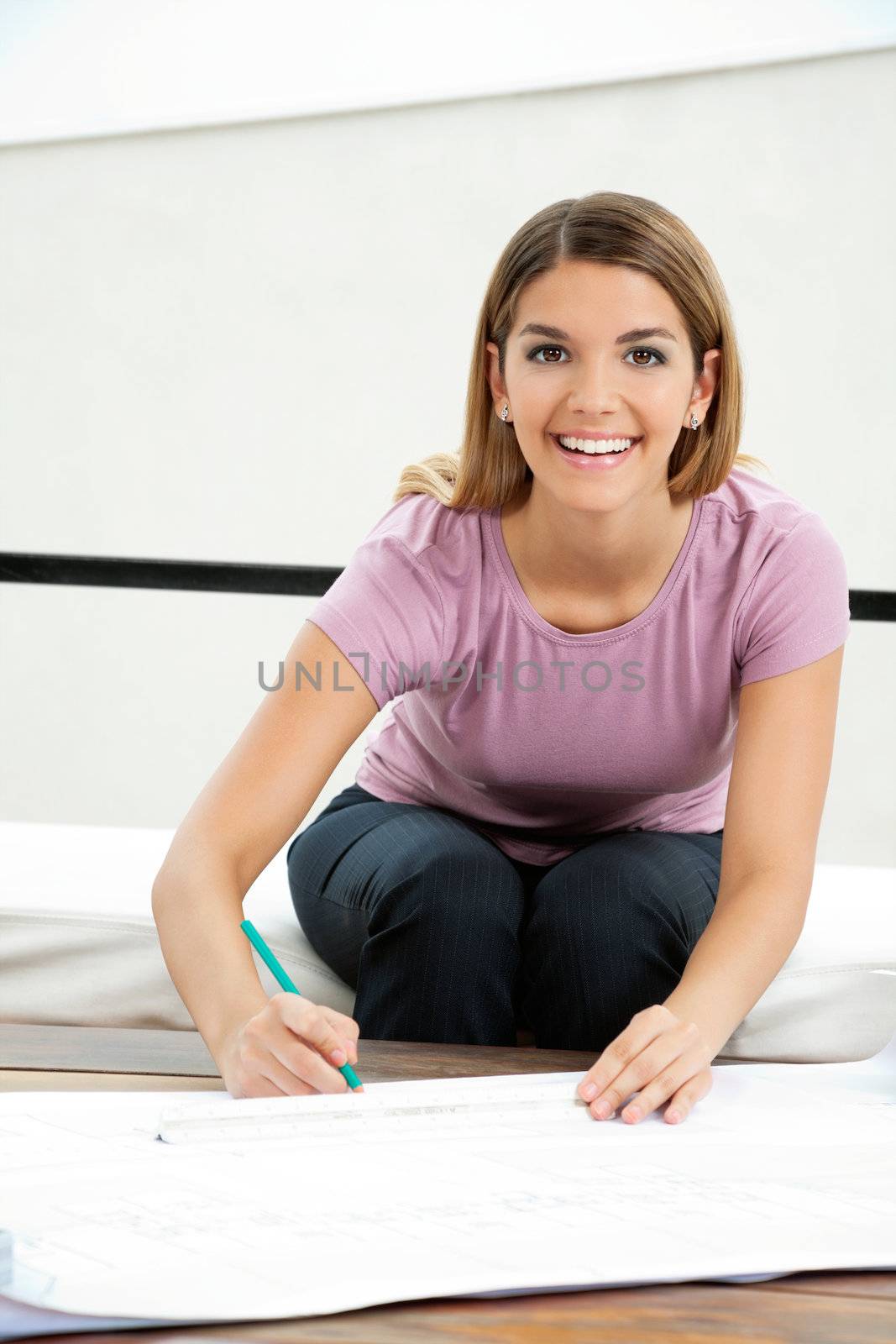 Portrait of pretty young female architect smiling while drafting blueprint