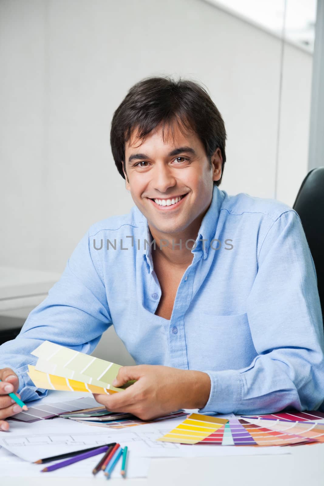 Portrait of young male interior designer smiling while holding color swatches
