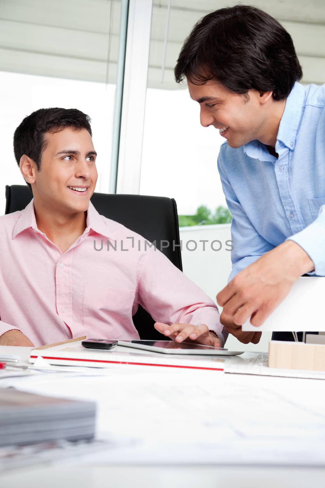 Young male architect looking at colleague while sitting in office chair