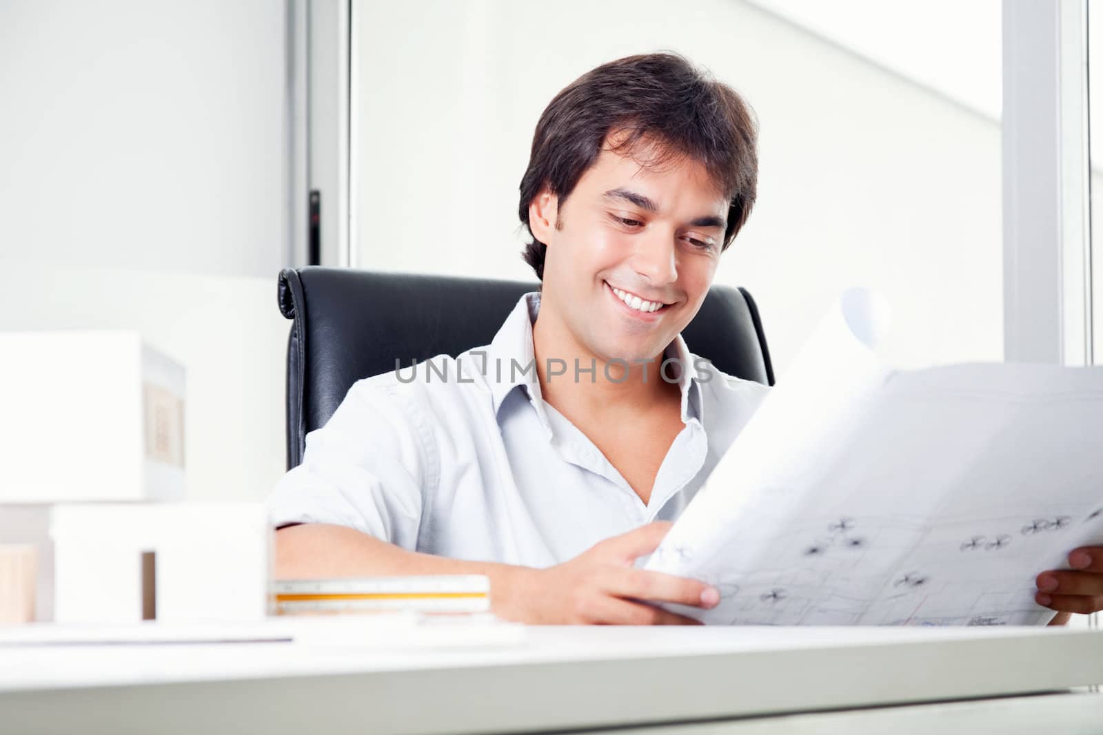 Smiling happy architect looking at blueprints in office.